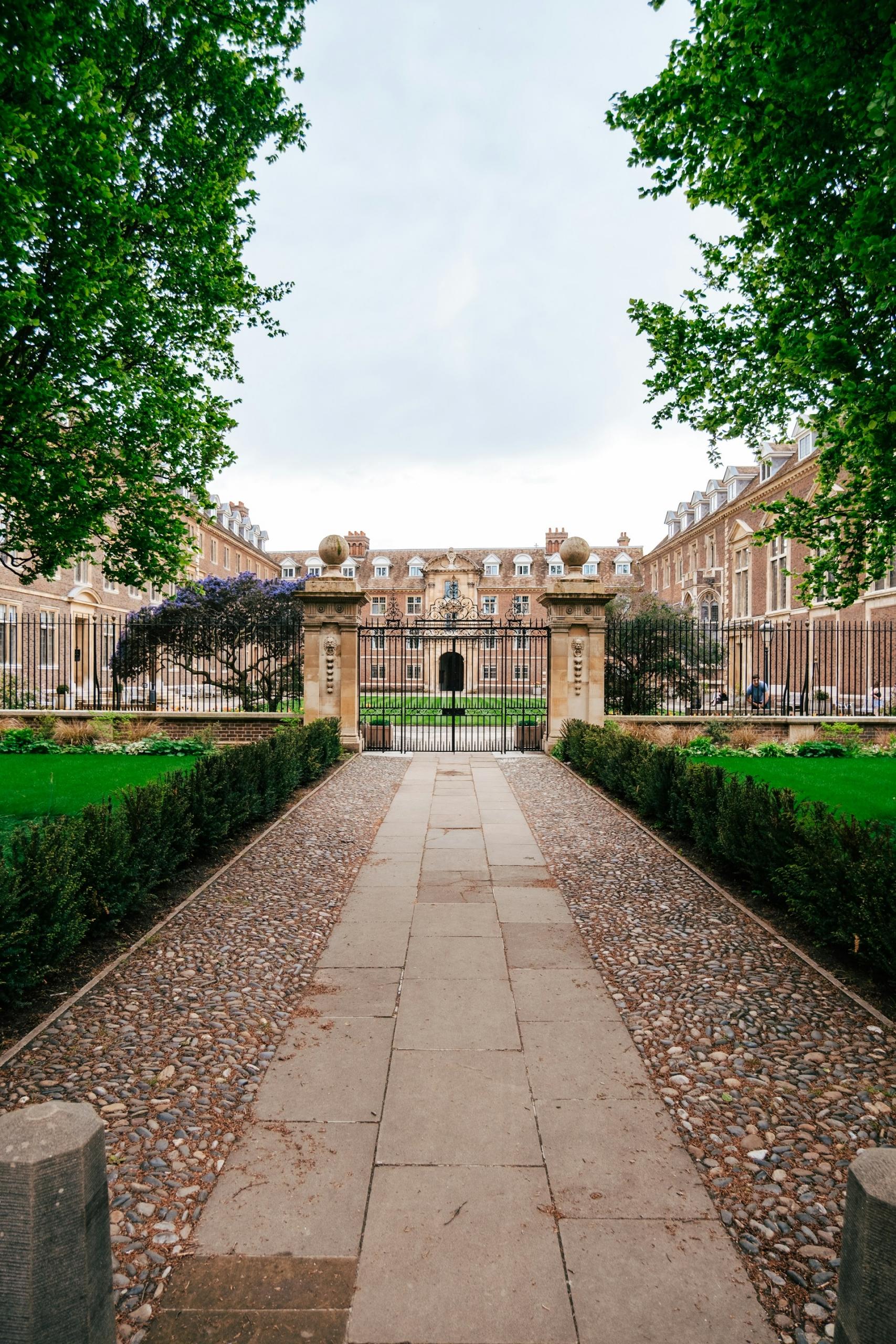 A long paved walkway leading to a stone building on a cloudy day.