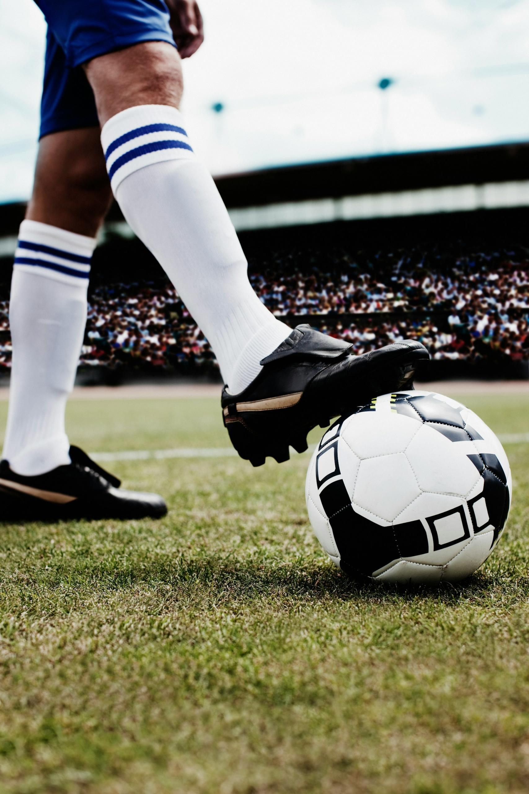 A Player rests their foot on a soccer ball in a stadium. 