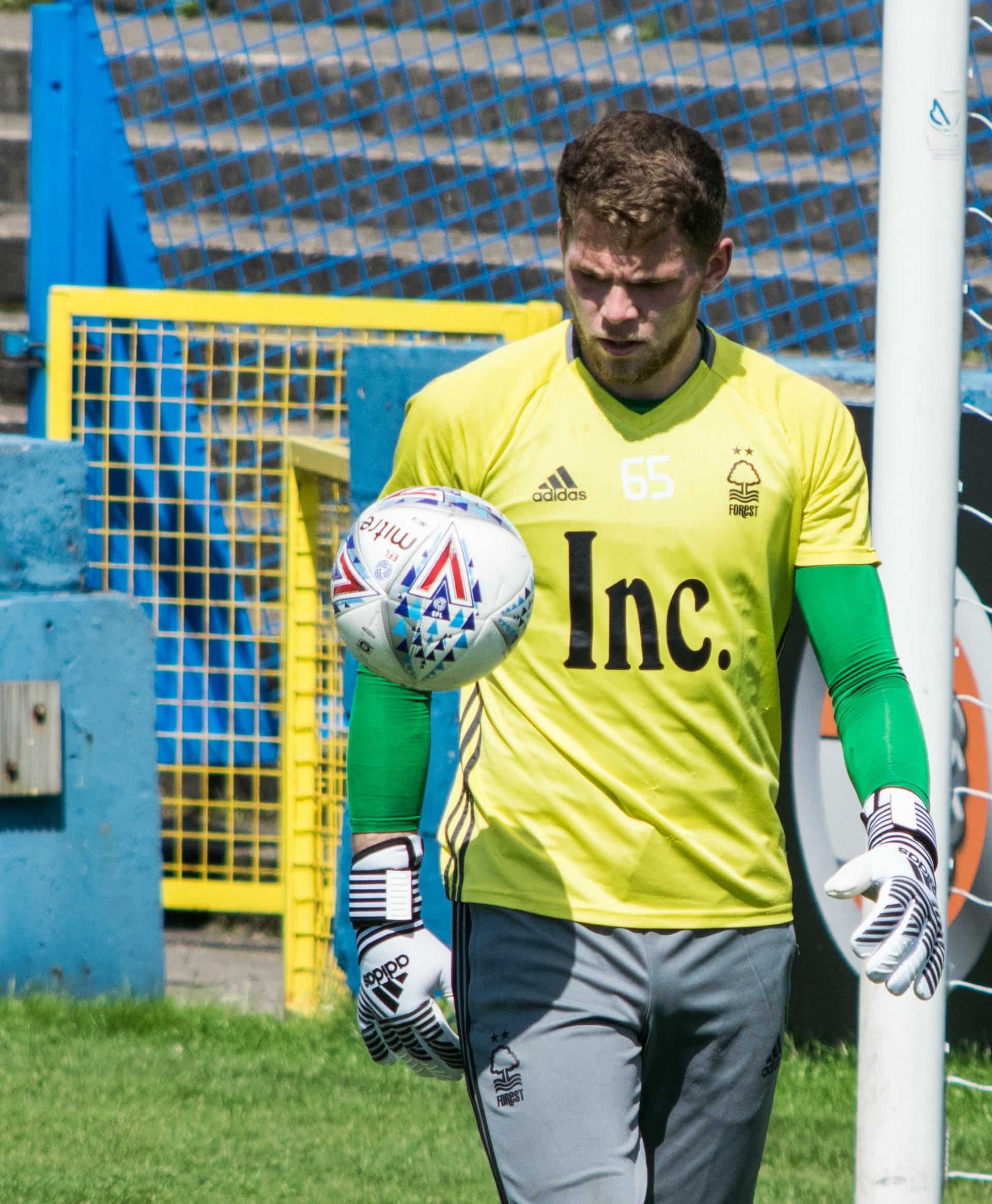 A man in a yellow jersey looks at a soccer ball on a sunny day. 
