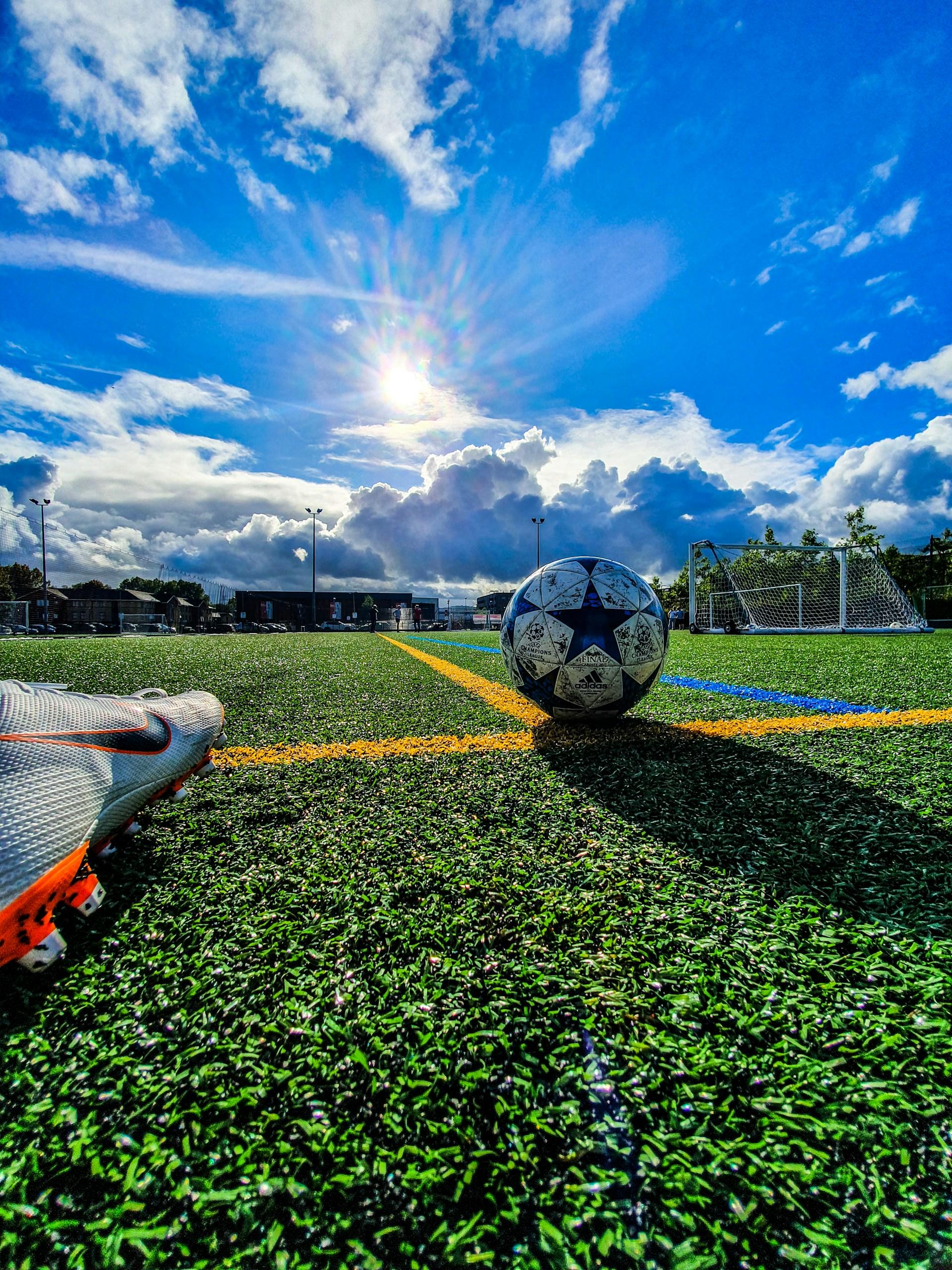 A football rests on a pitch line on a sunny day. 