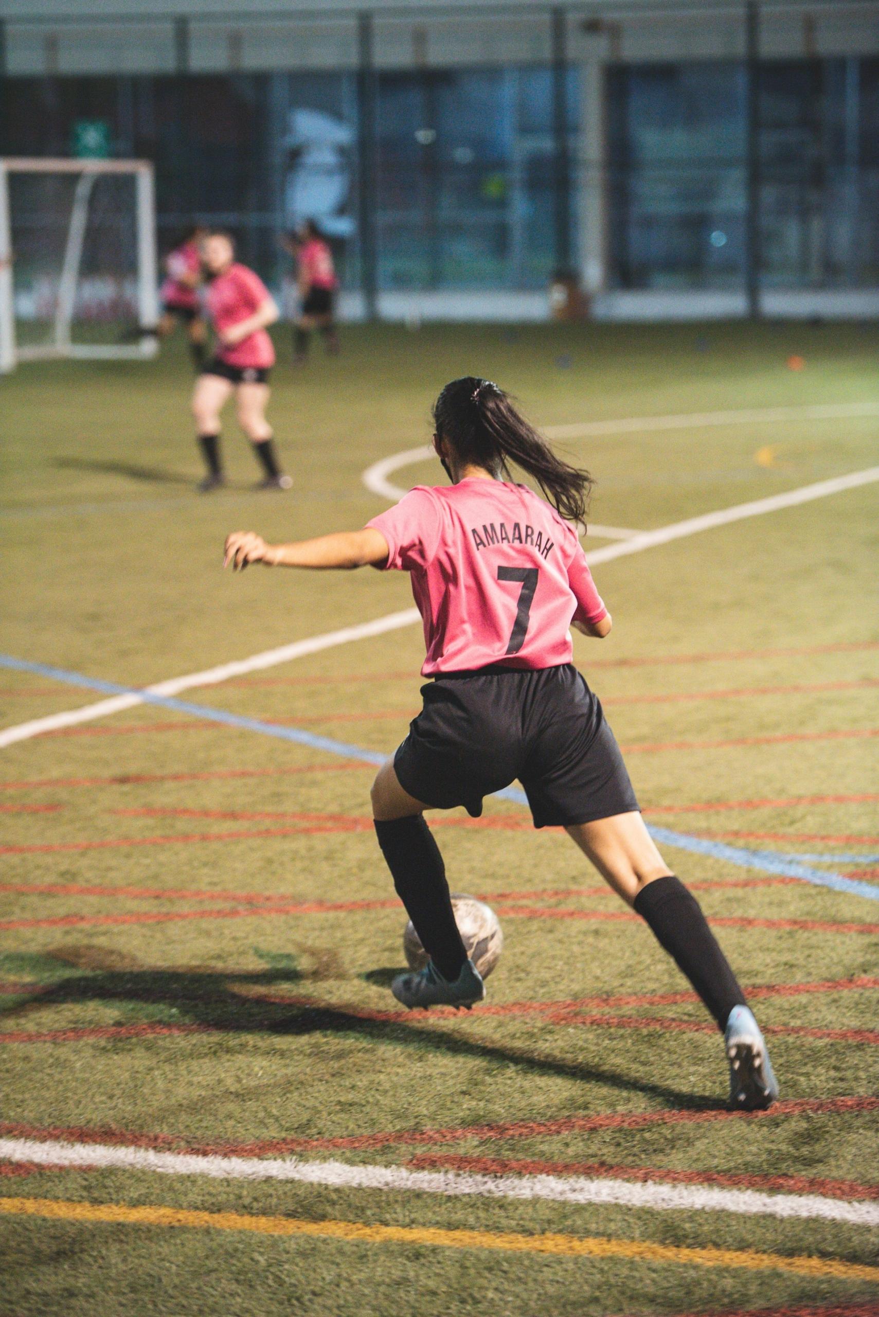 Girls playing football at night on a lit-up pitch. 