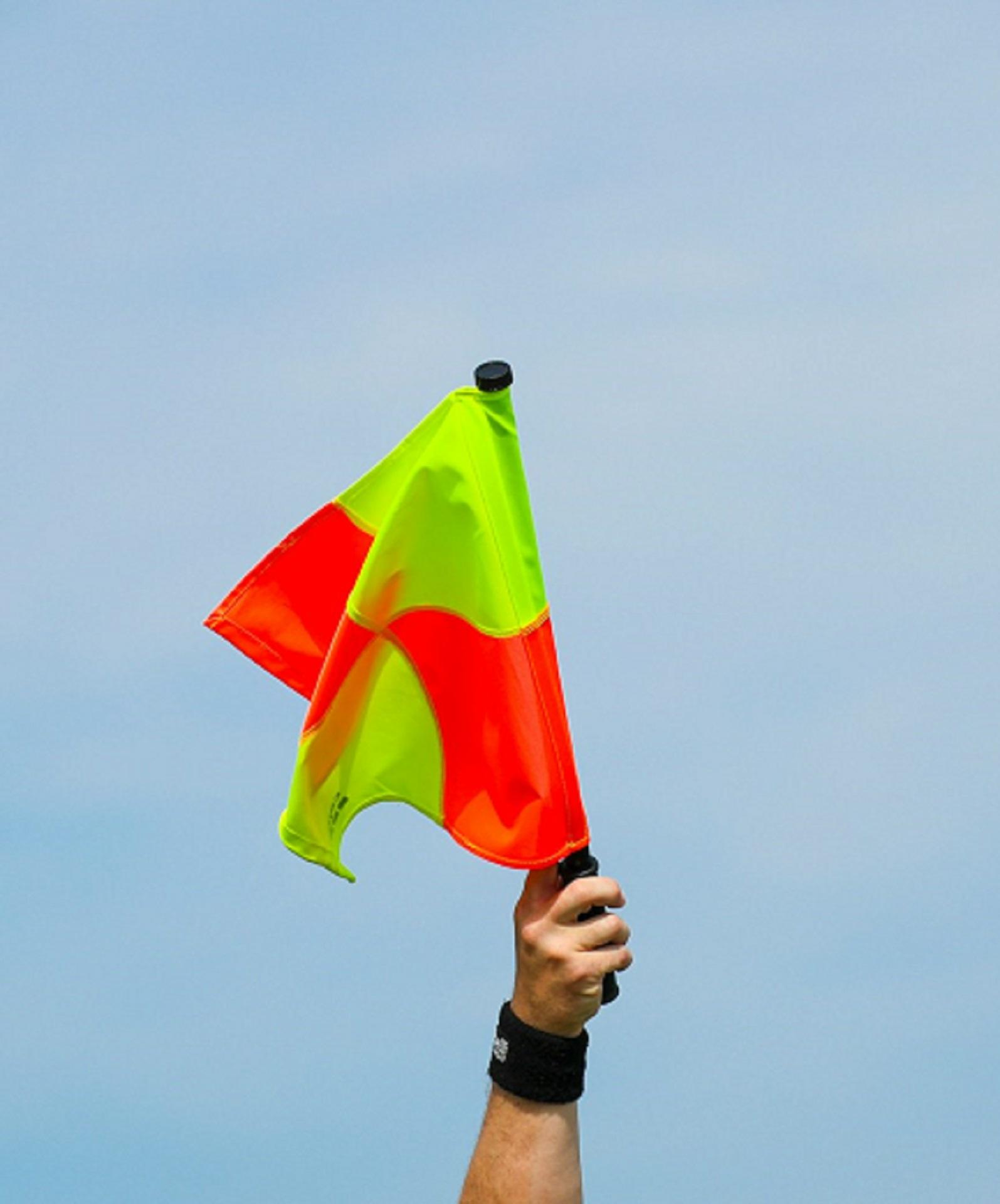 A hand holding a yellow and orange flag in the air.