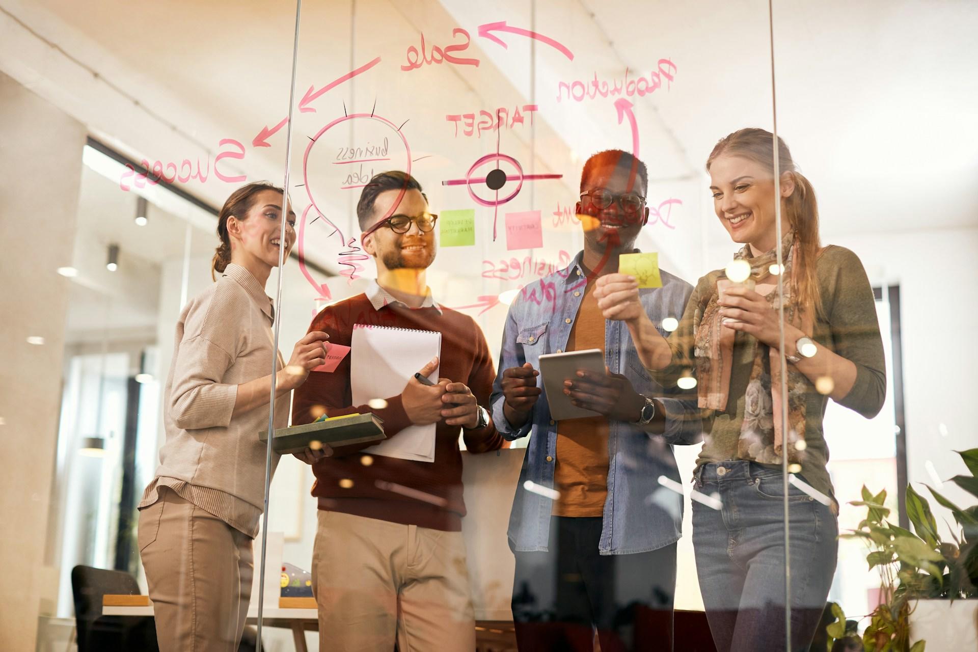 A diverse group of people standing in front of a glass wall, working on a problem.
