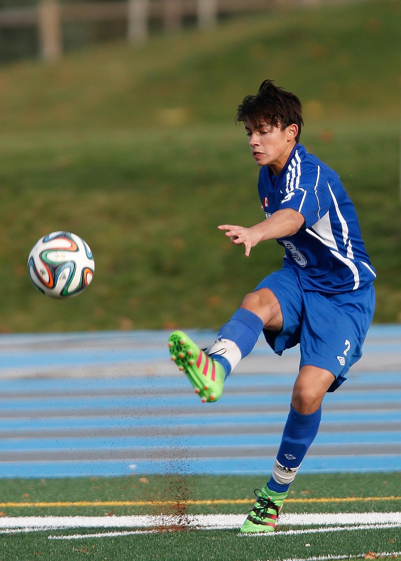 A person in a blue team outfit kicks a soccer ball.