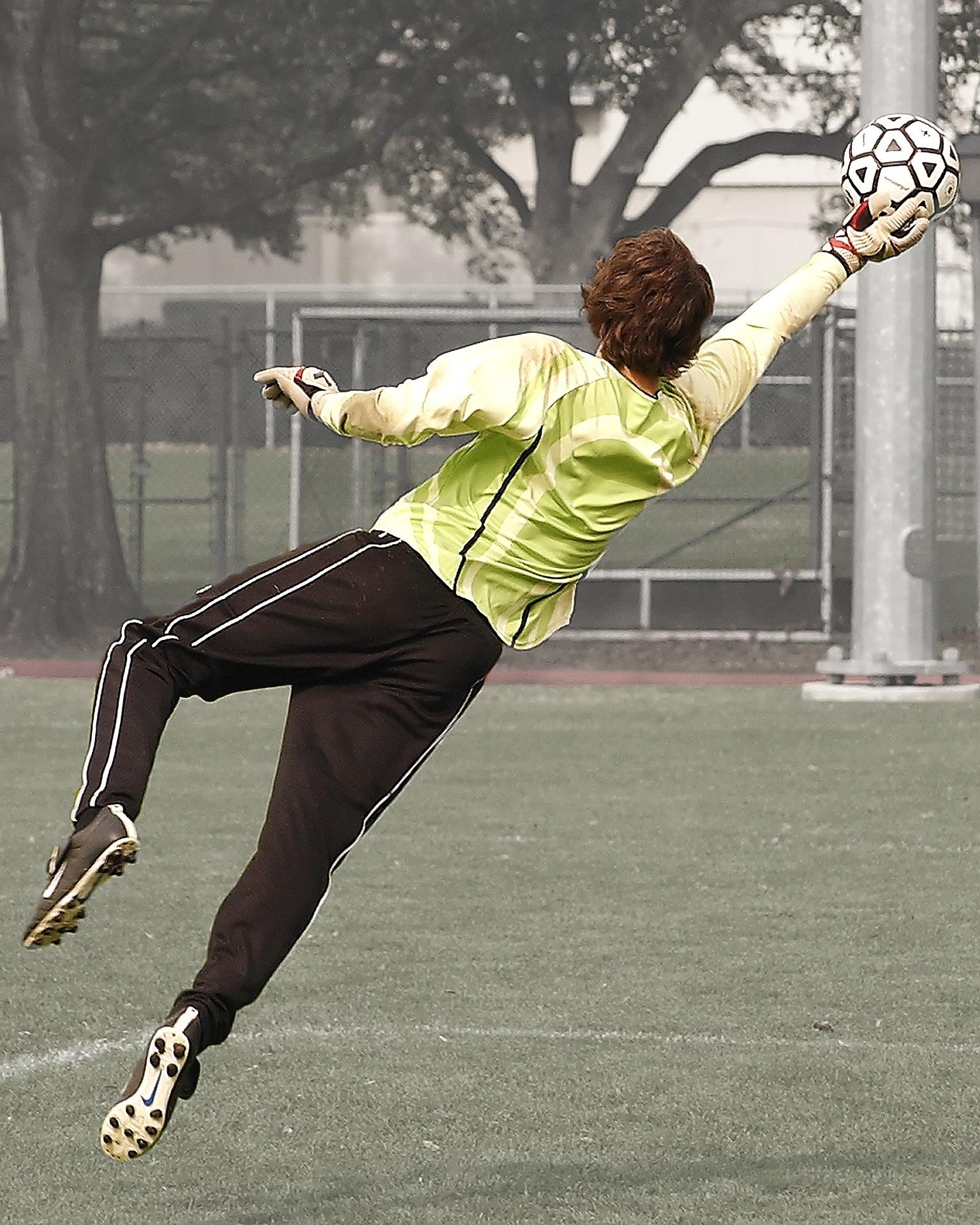 A person in a goalie uniform catches the ball in mid-air.