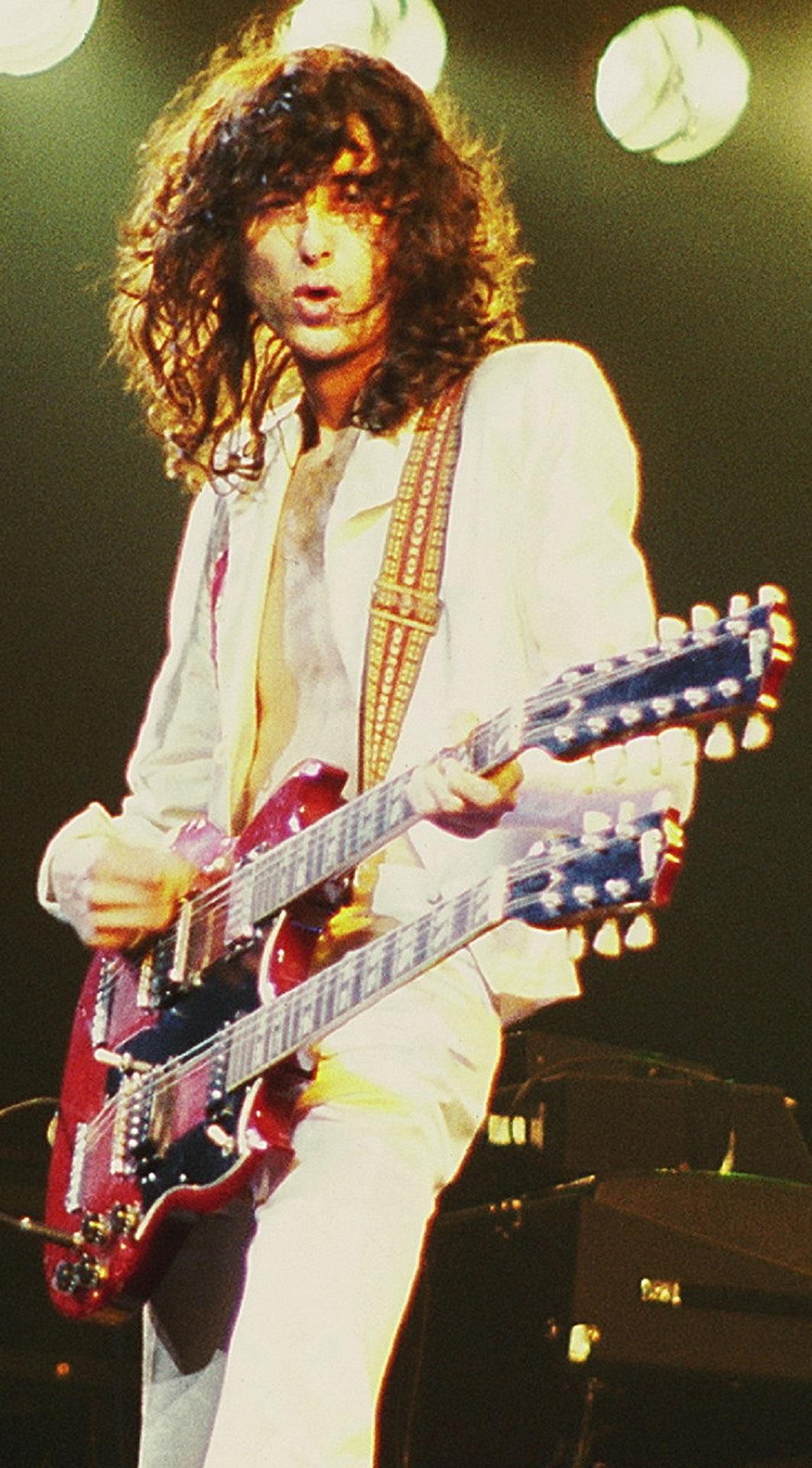 A man wearing white plays a double guitar on stage. 