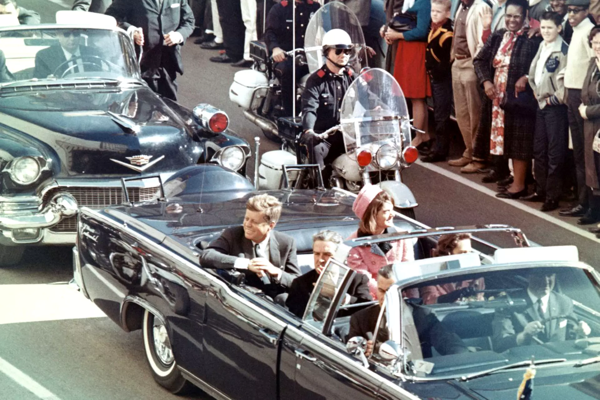 JFK driving in a convertible car amongst a crowd