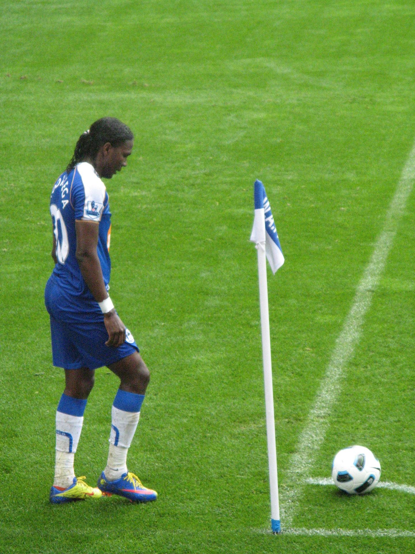 A man in a blue uniform stands by a flag and a soccer ball.