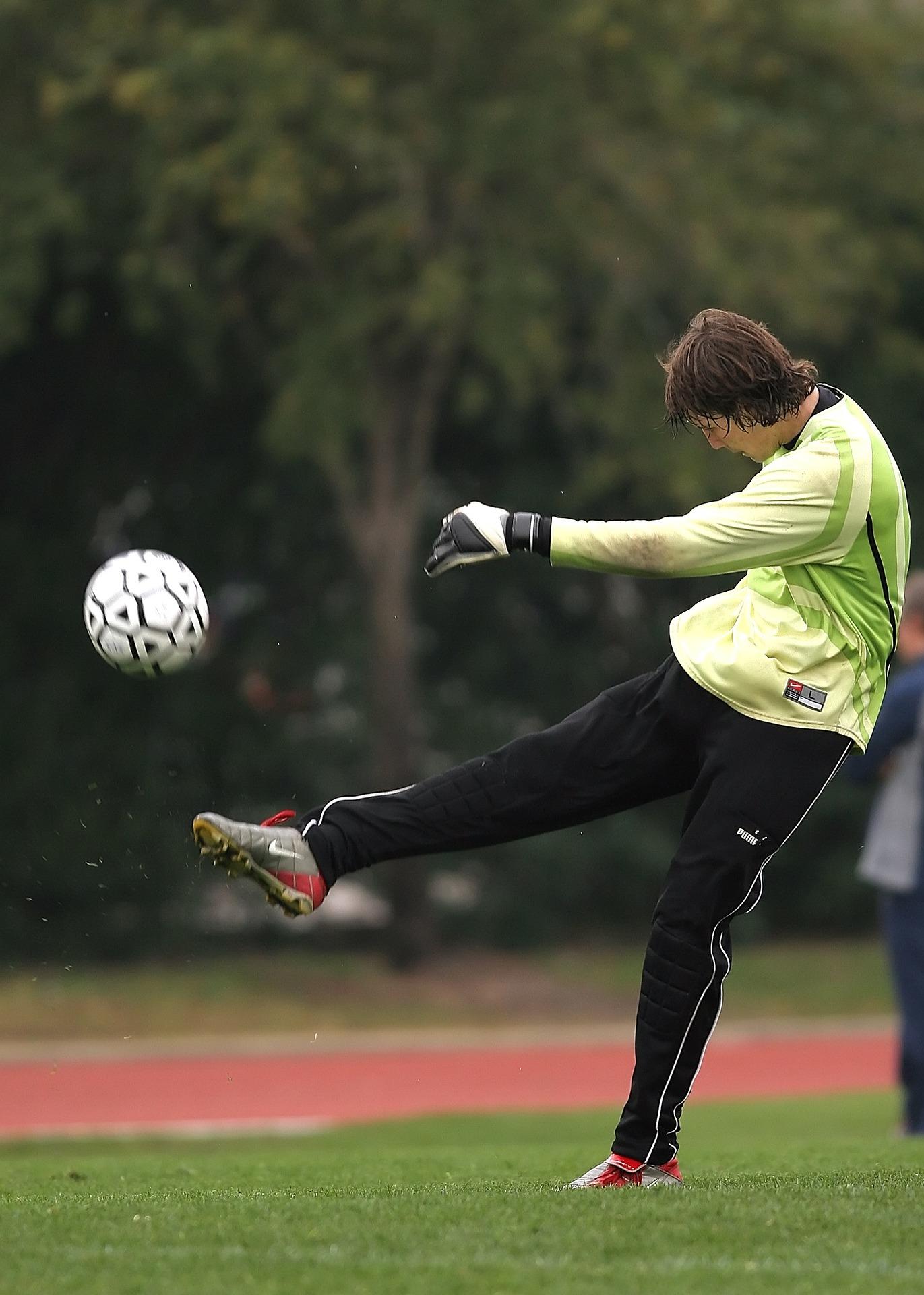 A person wearing yellow and black sports outfit kicks a soccer ball.