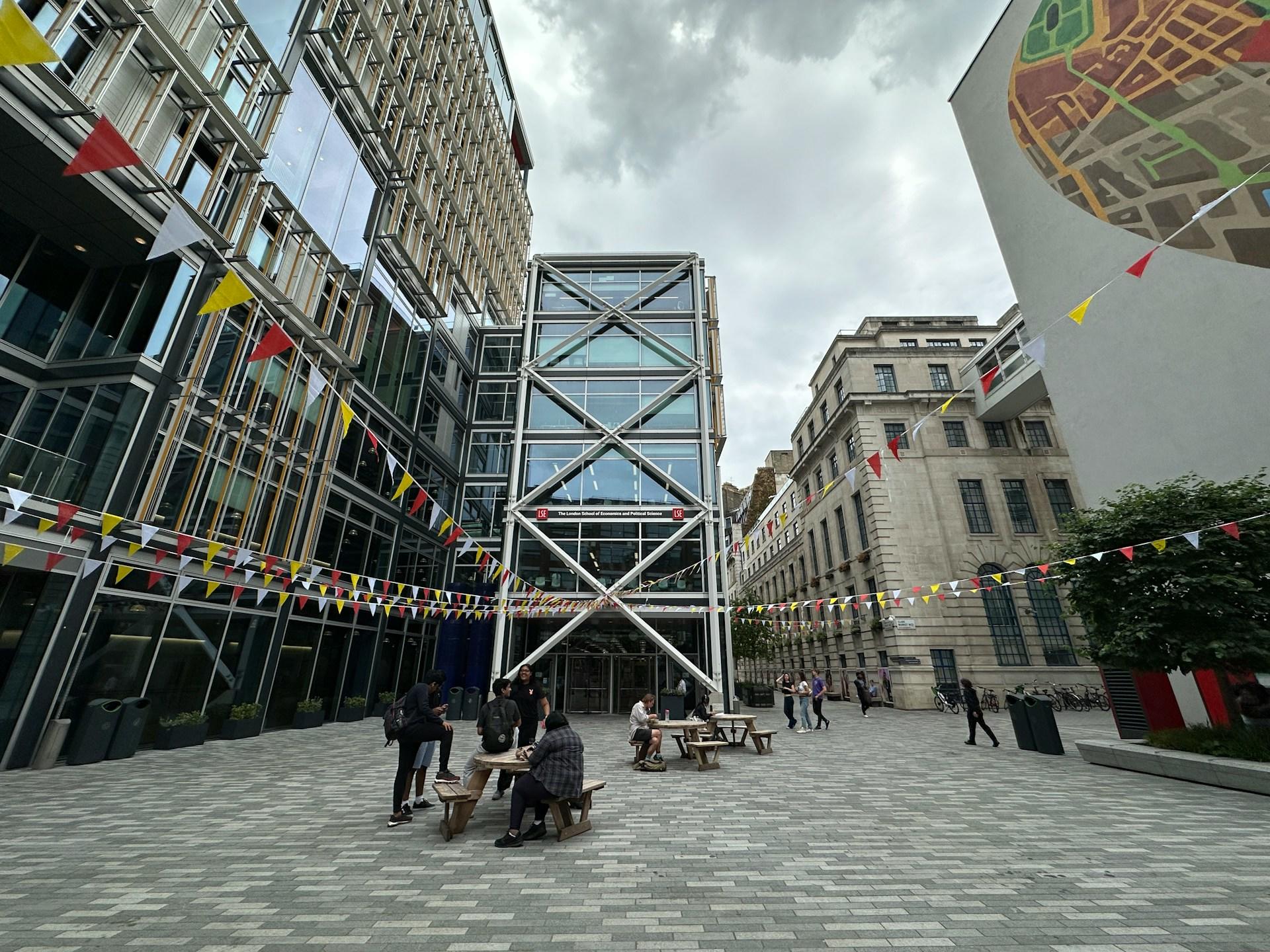 Glass fronted buildings surrounding a paved area with people present on a cloudy day.