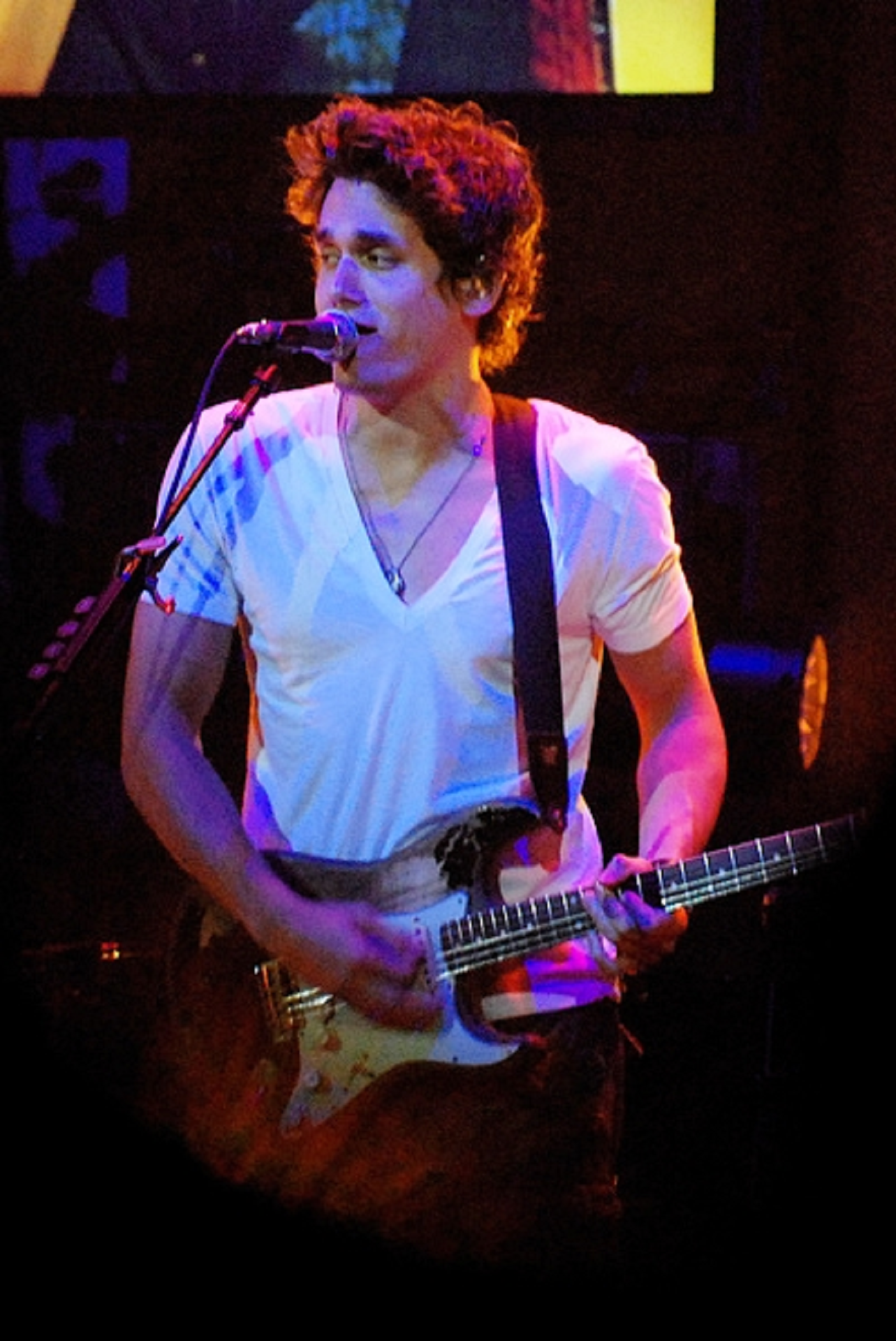 A man in a white shirt plays guitar and sings. 