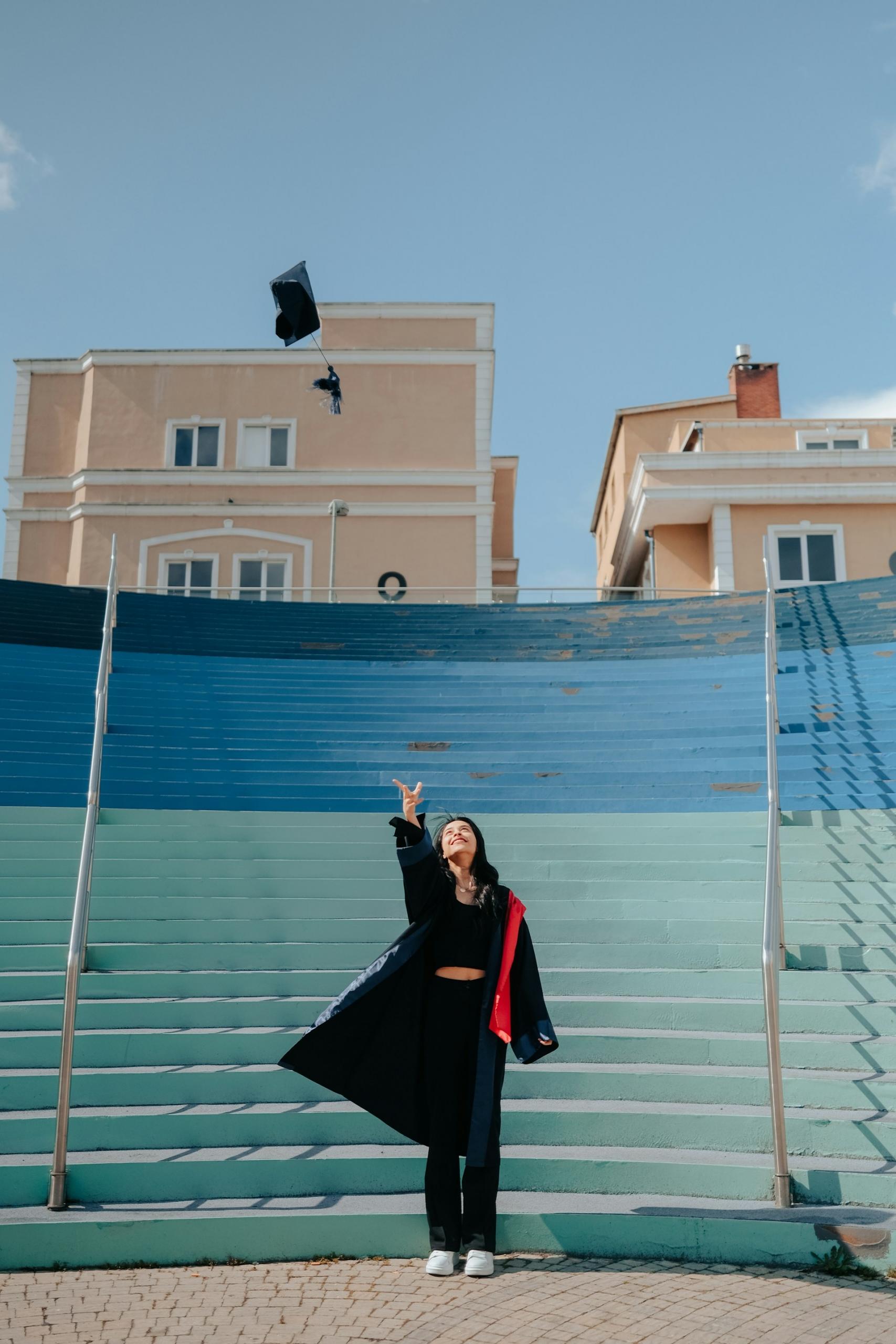 A person wearing graduation regalia in front of blue steps on a sunny day.