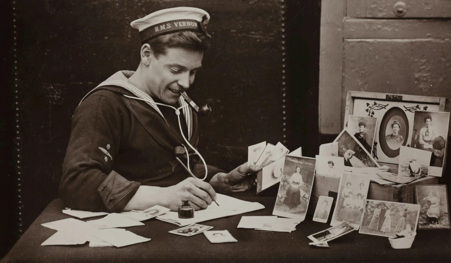 A greyscale of a man in uniform sitting at a desk with pictures and papers on it.
