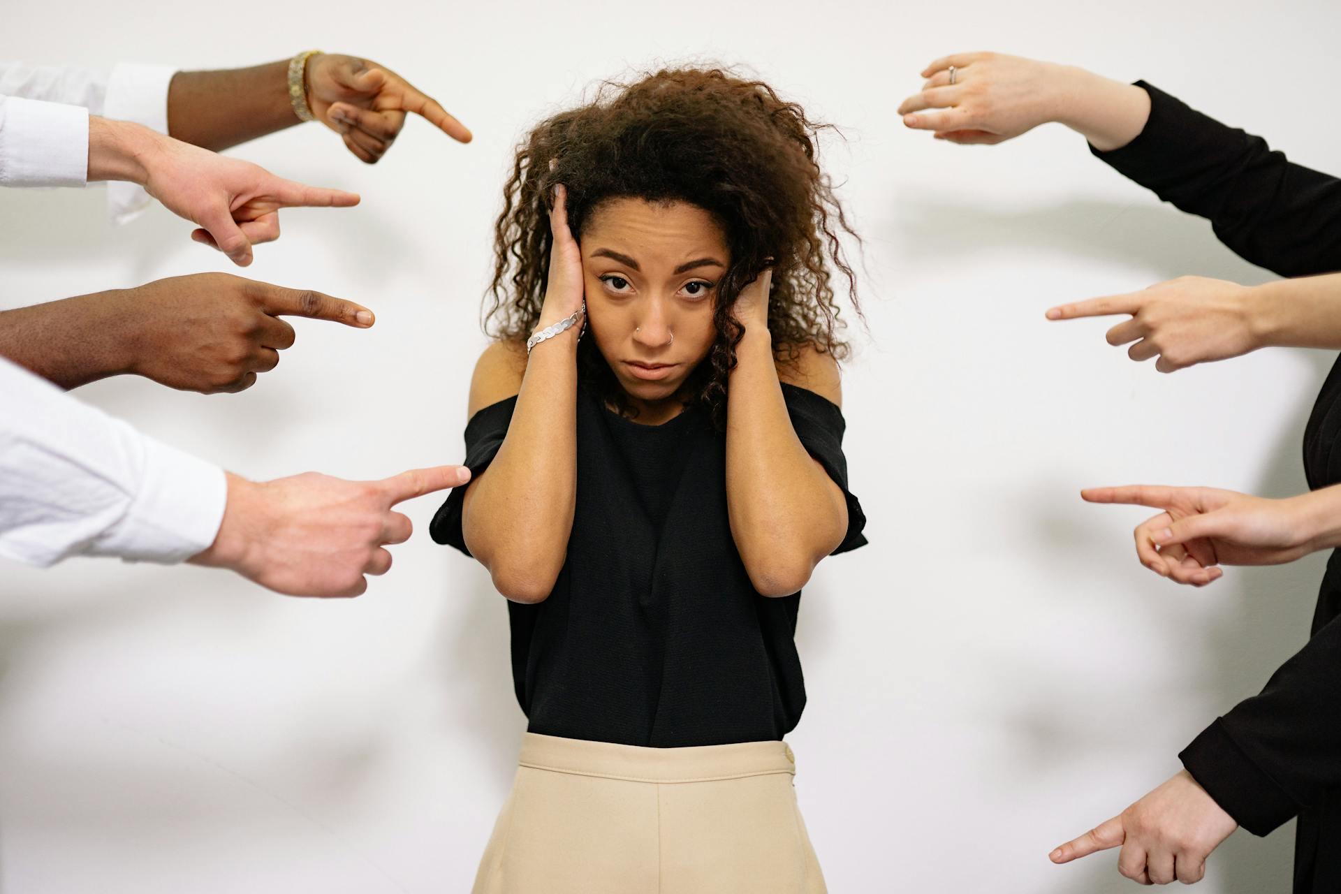 A woman covering her ears while people point at her.