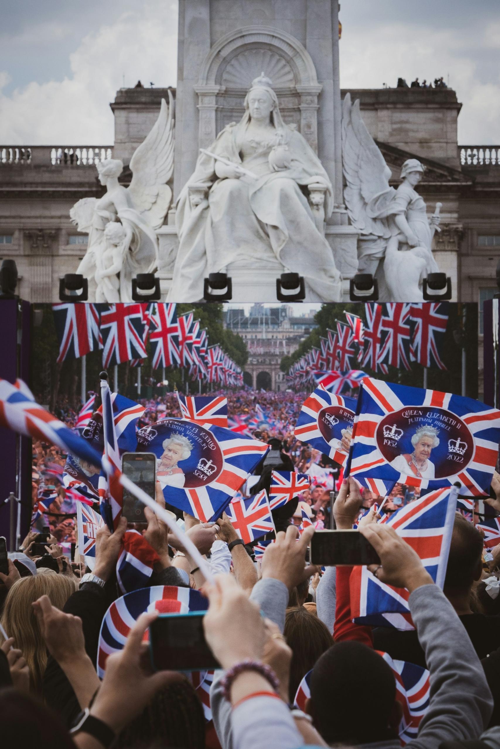 Many people and British flags gathered in front of a statue.