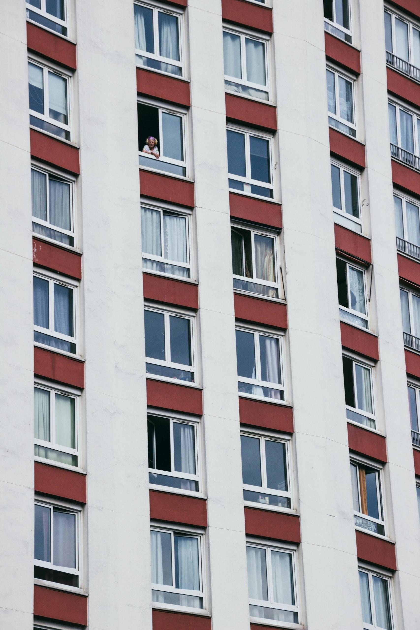 A white and red building, with lots of windows, and a person looking out one window. 