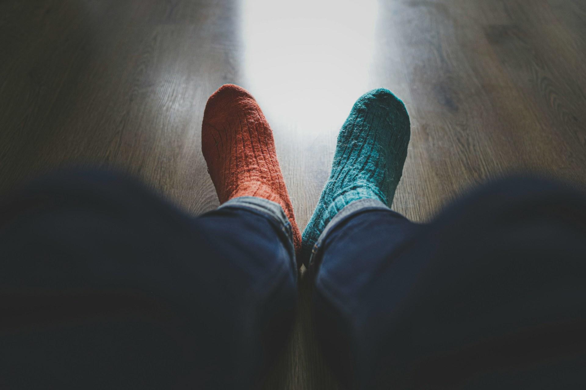 Odd socks on feet on wooden flooring.