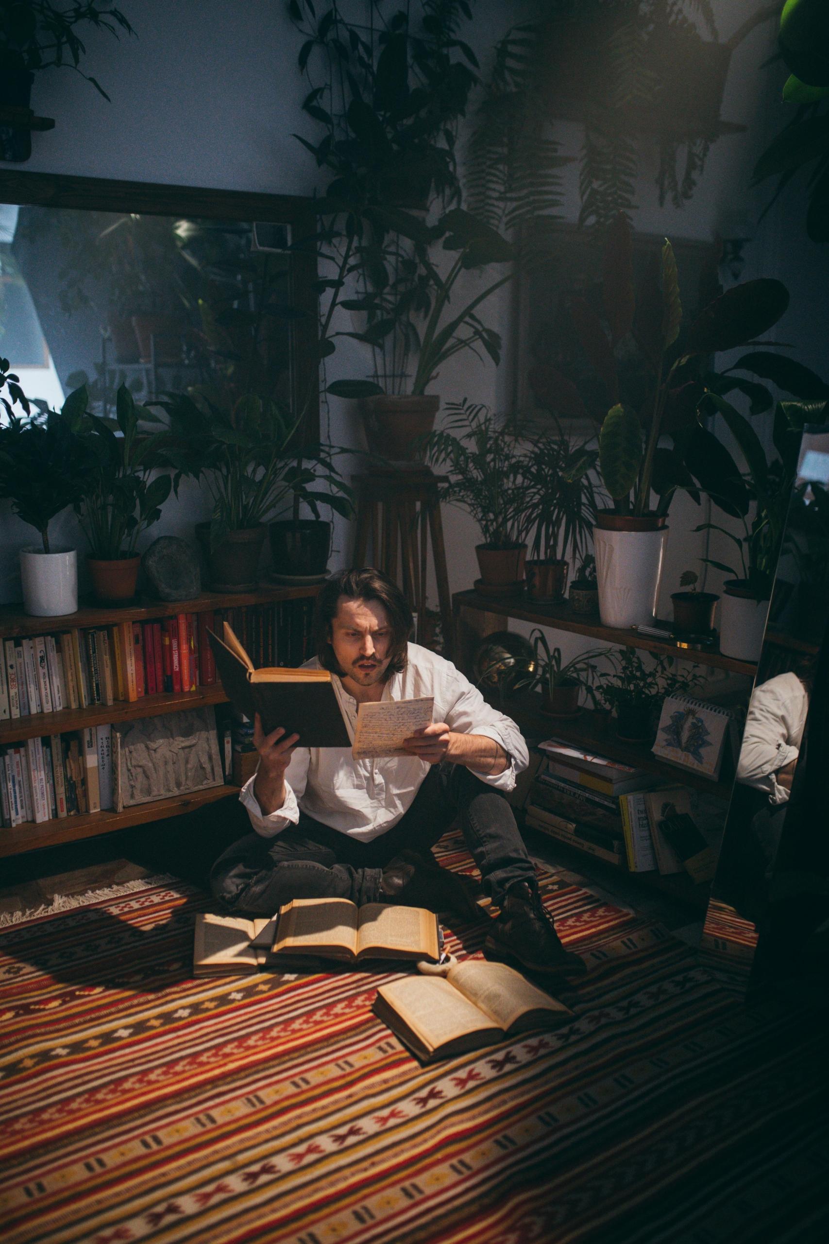 A poet is sat on his floor, reading the work of other literary minds for some inspiration