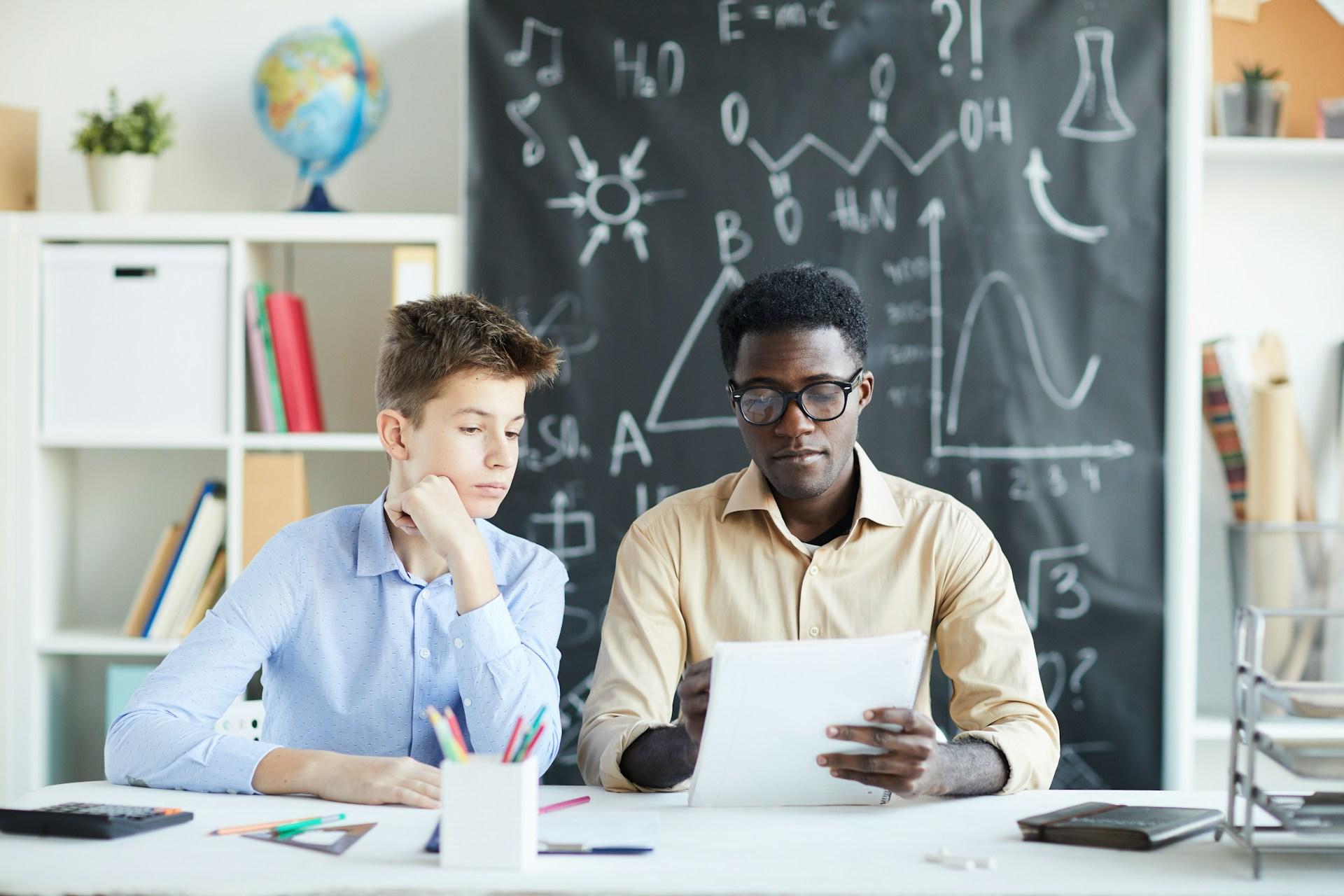 A man wearing glasses holds a paper while a boy in a blue shirt looks on. 