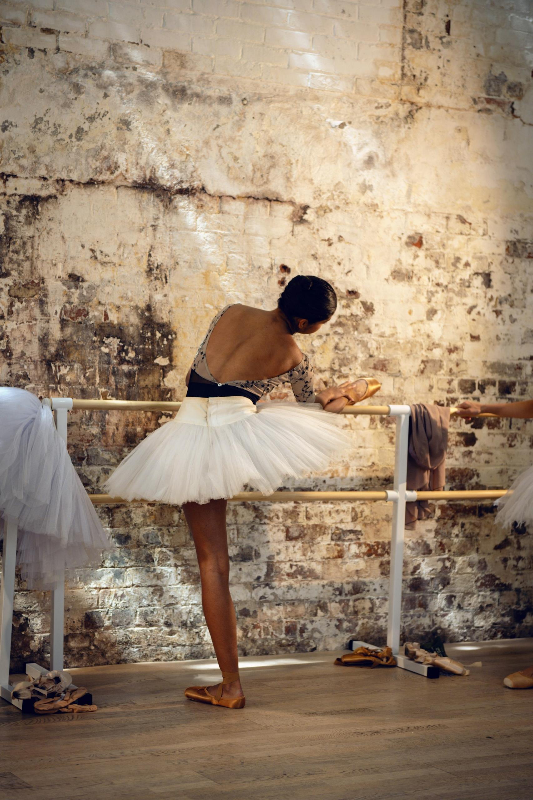 A woman in a white tutu and a foot on a ballet barre.