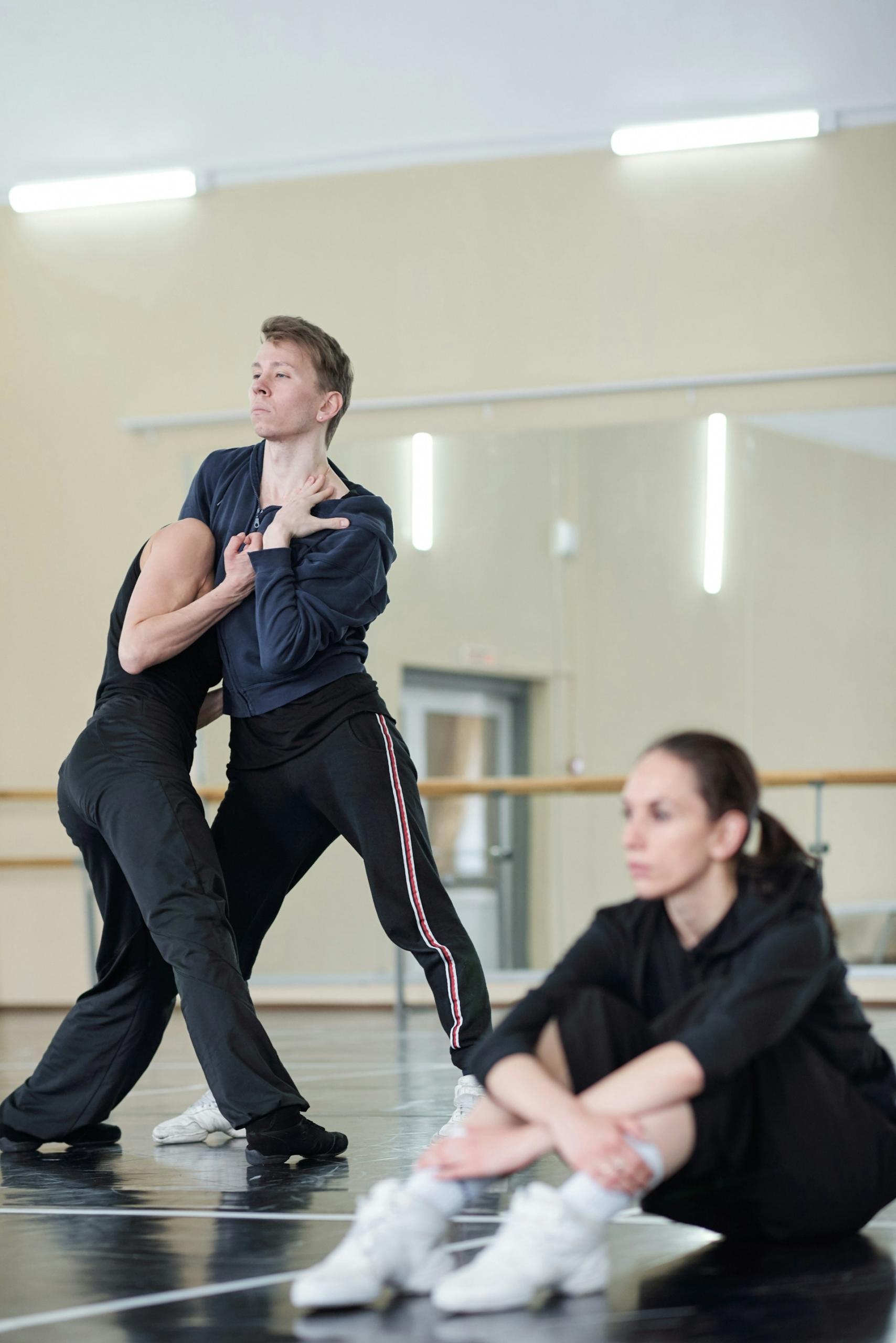 Two people dance in a studio while another sits on the floor.