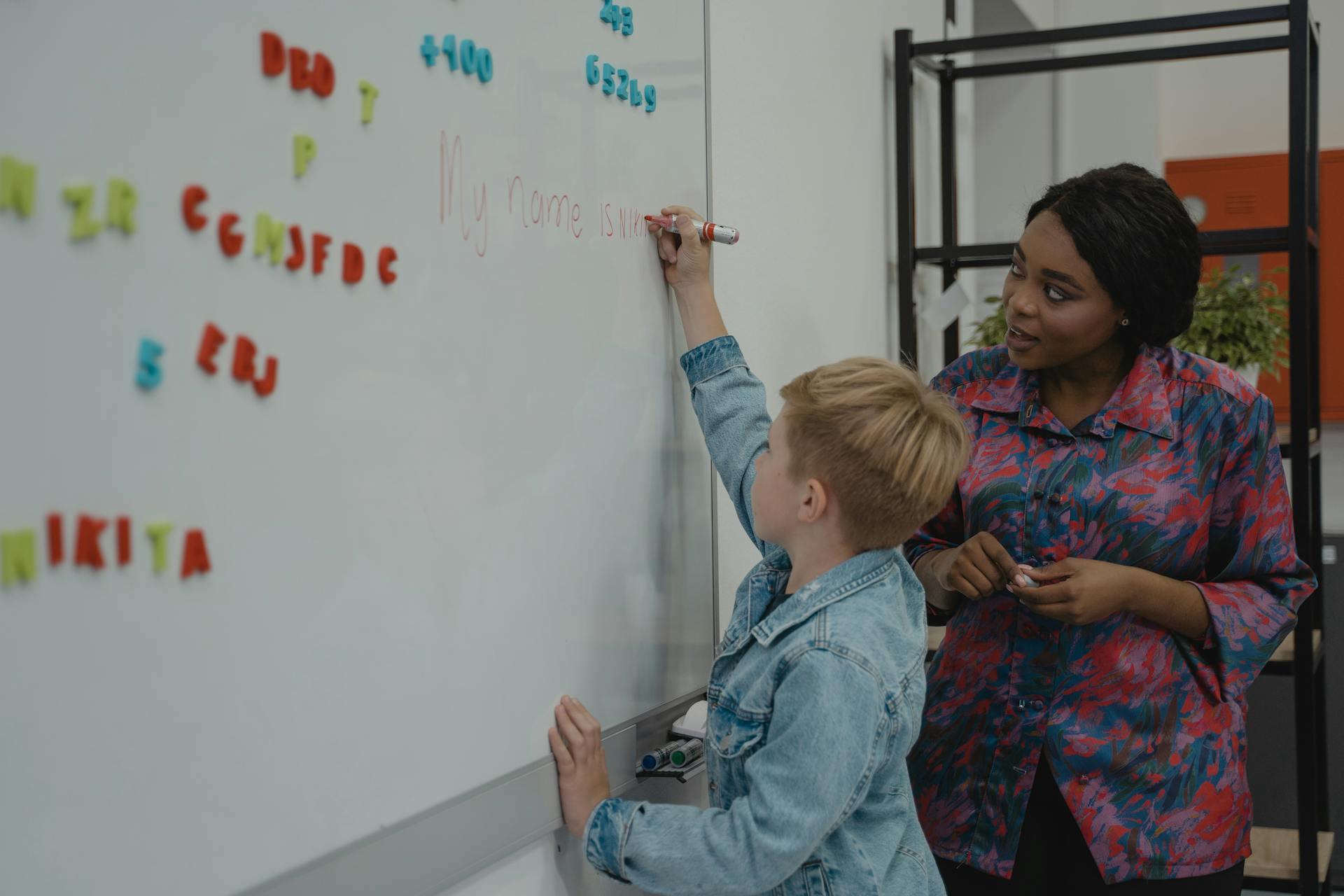 Young child writes on a whiteboard as part of a class activity.