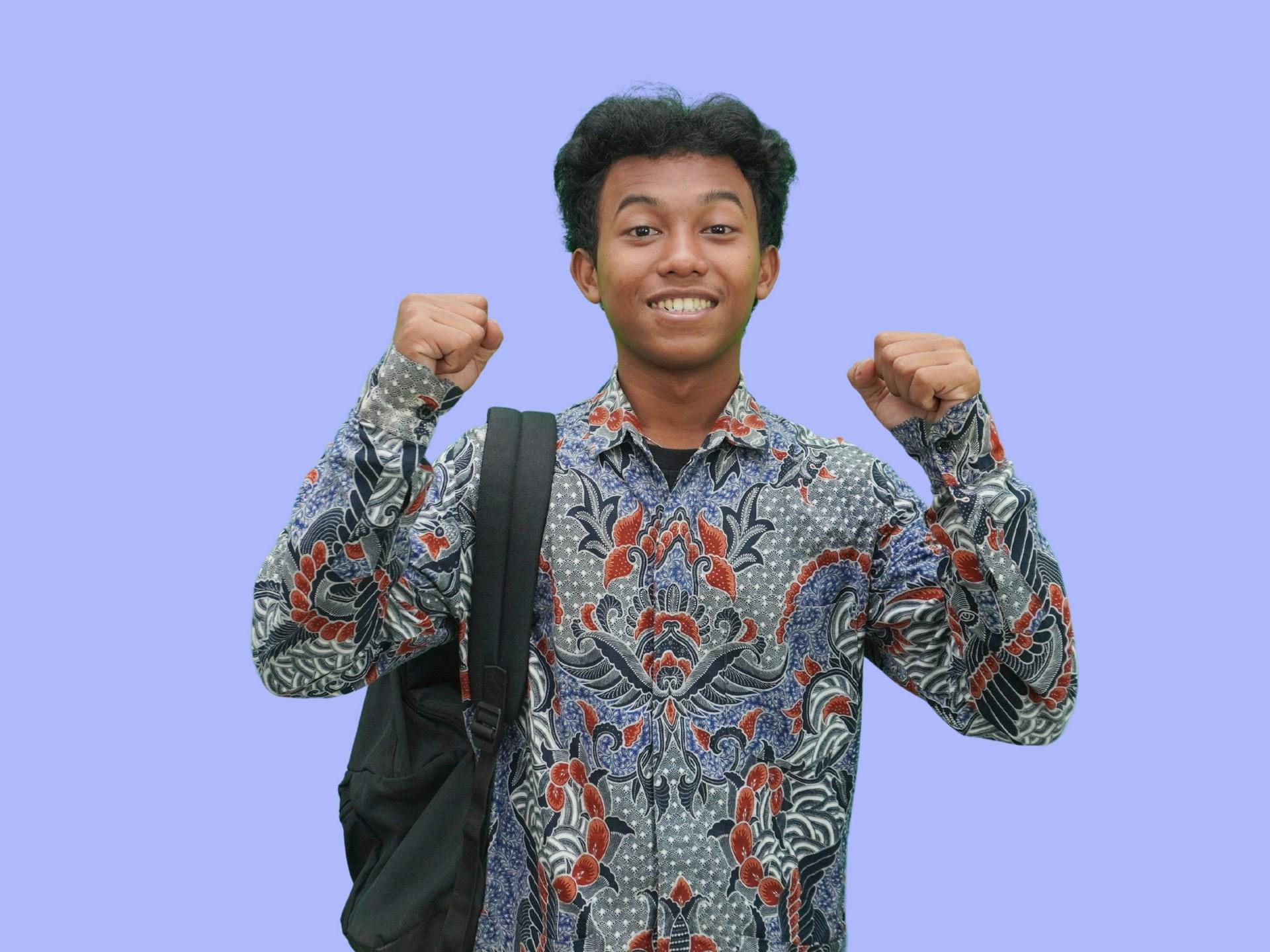 A person in a multi-coloured shirt smiles and holds their clenched fists up in victory while smiling.