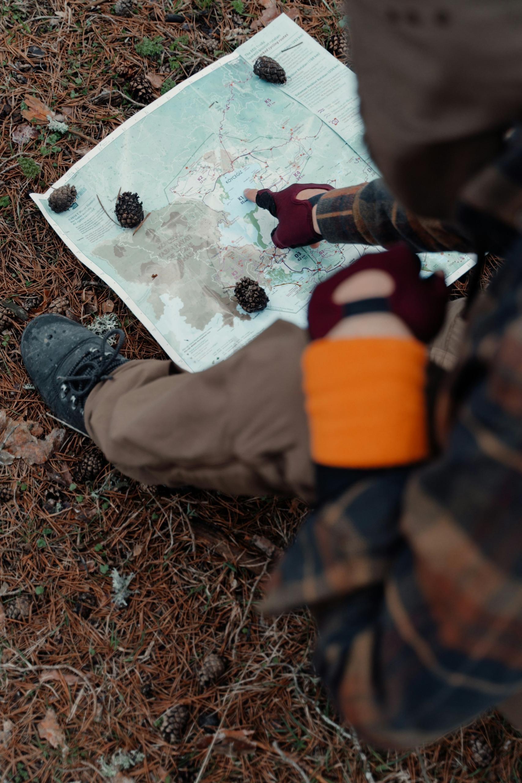 A person wearing red gloves points at a map on the ground.