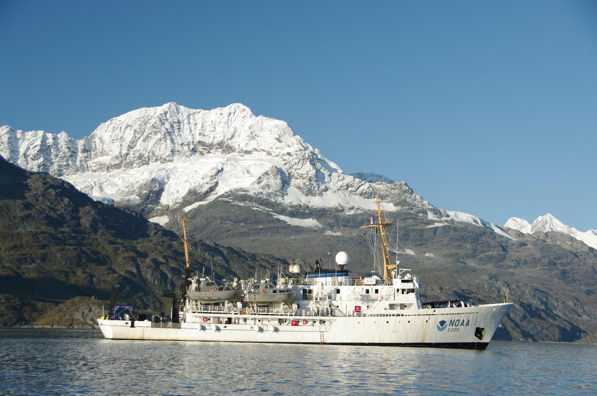 A ship in the water in front of a snow capped mountain on a sunny day.