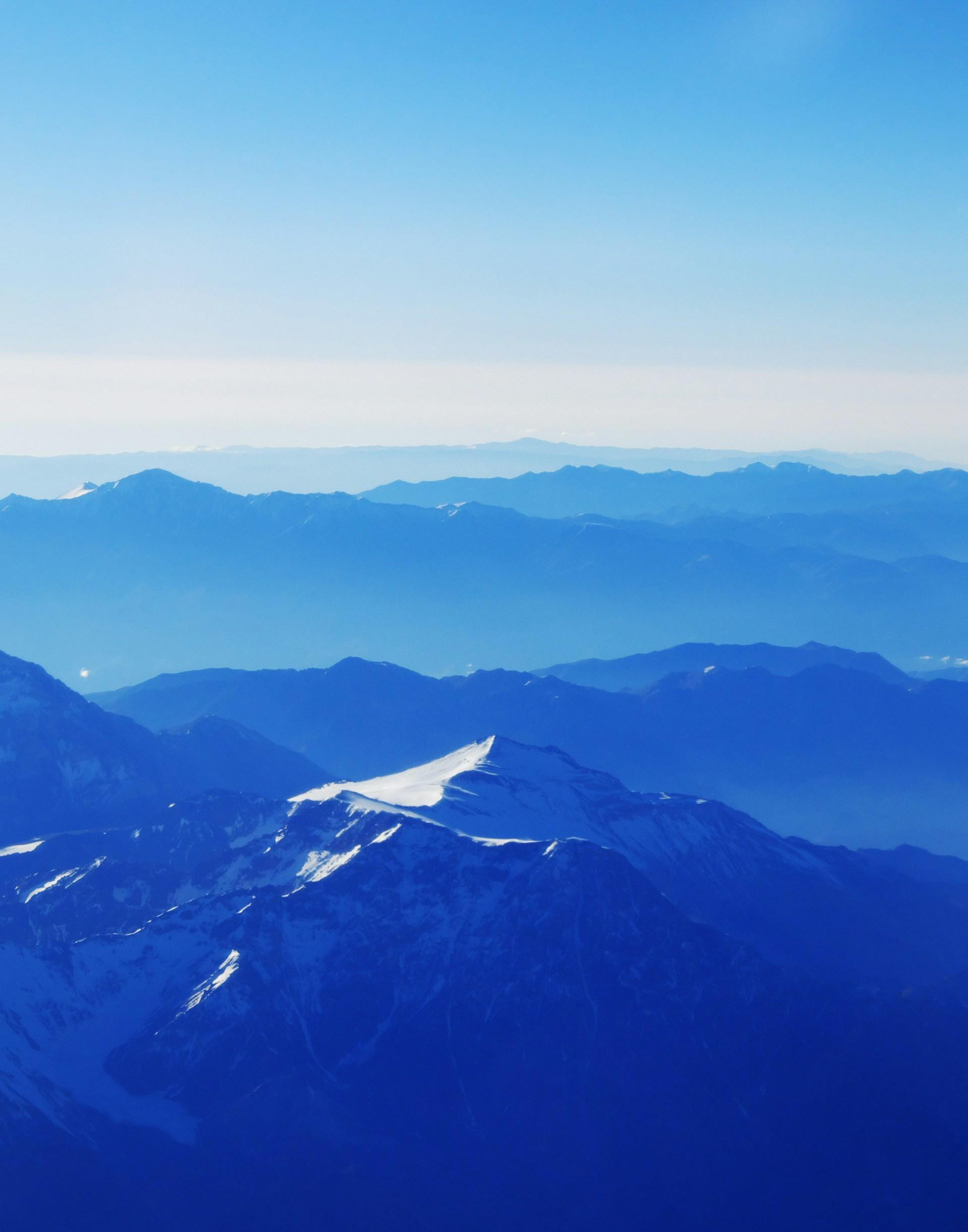 A snow-capped mountain range seen from the air, through a blue filter. 