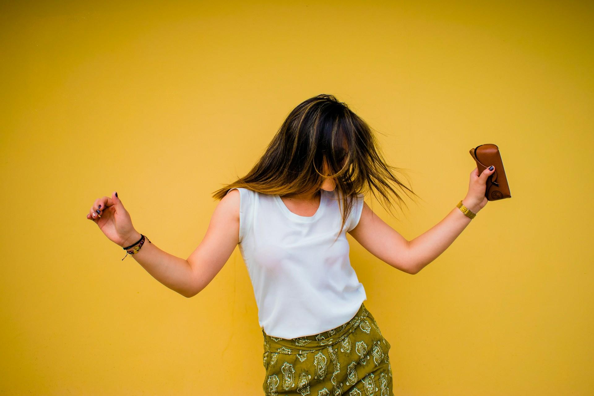 A woman in a white top dances against a yellow background.