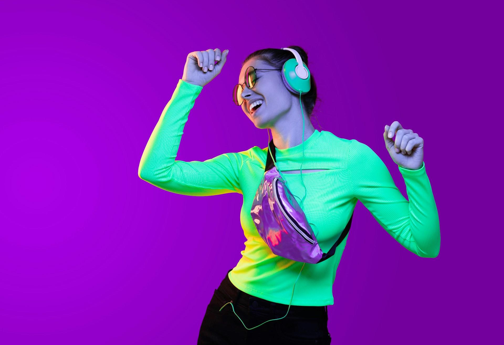 A woman in a teal shirt wears headphones and smiles as she dances.