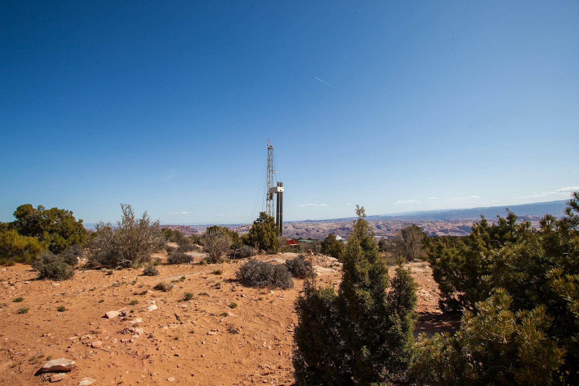 Desert scrubland with an oil rig in the distance on a sunny day.