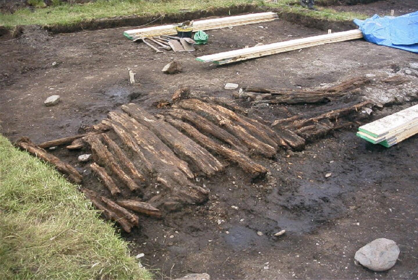 Several durable wooden beams lying next to each other in a dirt patch bordered by grass. 