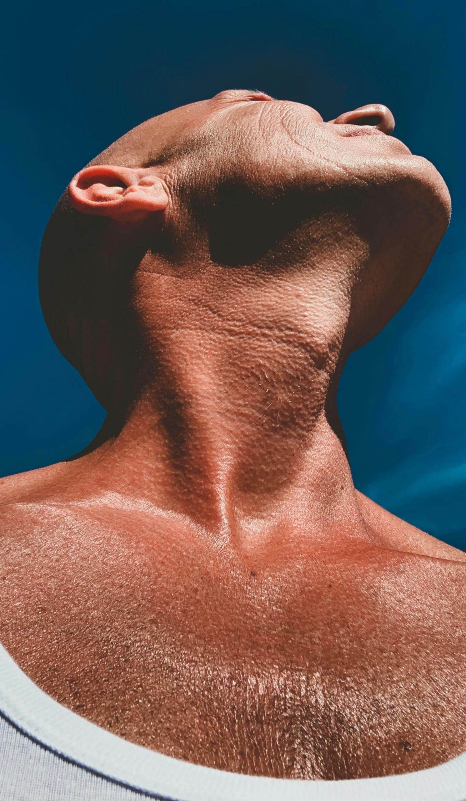 A man rolls his head back to stretch his neck on a sunny day. 