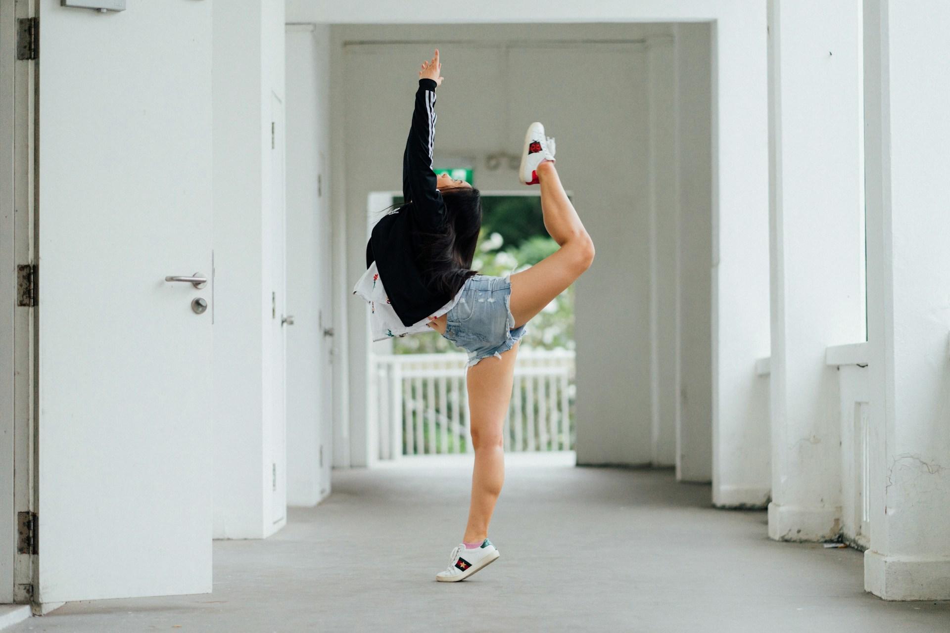 A woman wearing casual clothing holds a dance pose in an empty hallway.