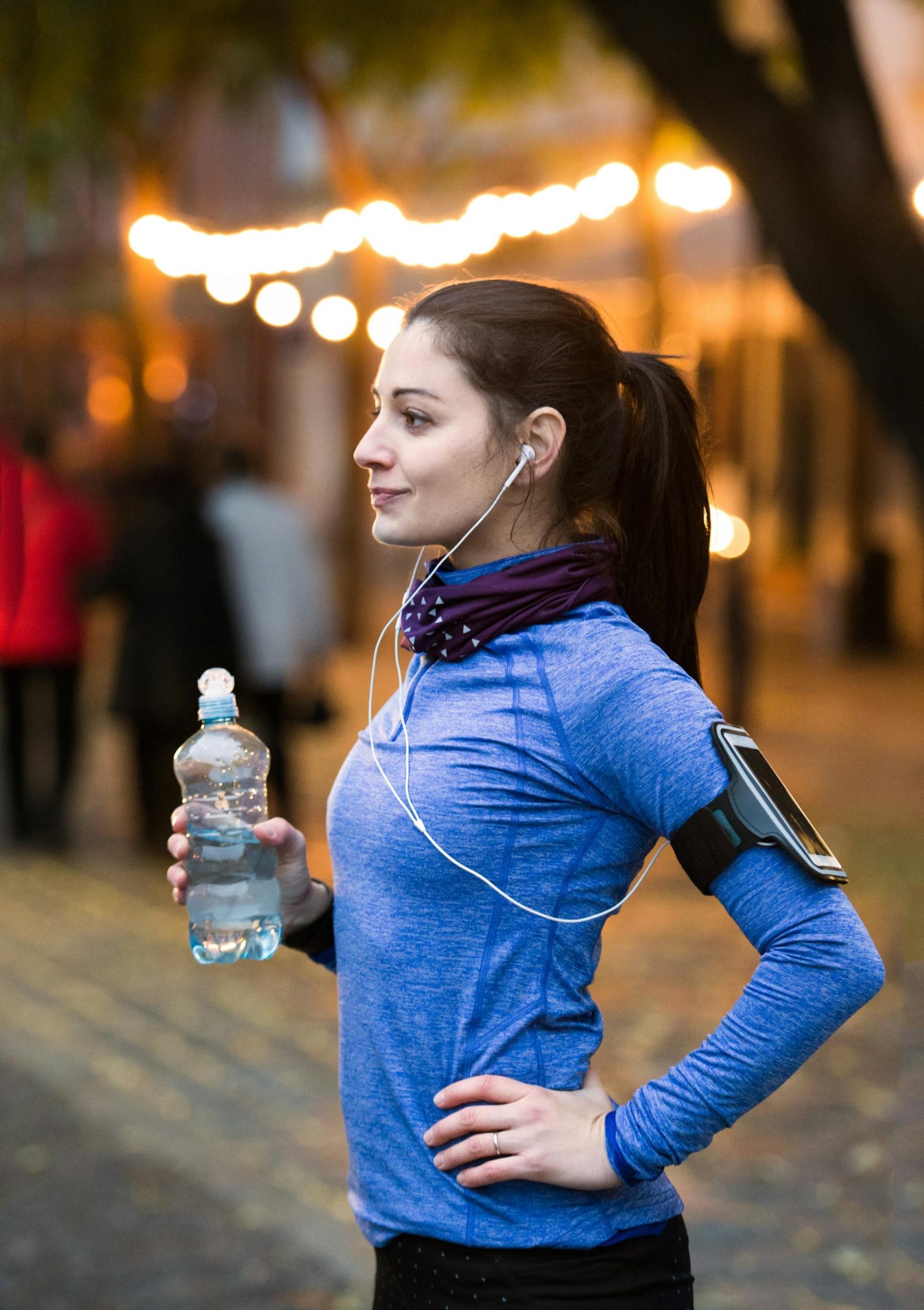 A woman in a blue top holds a water bottle and one hand on her hip. 