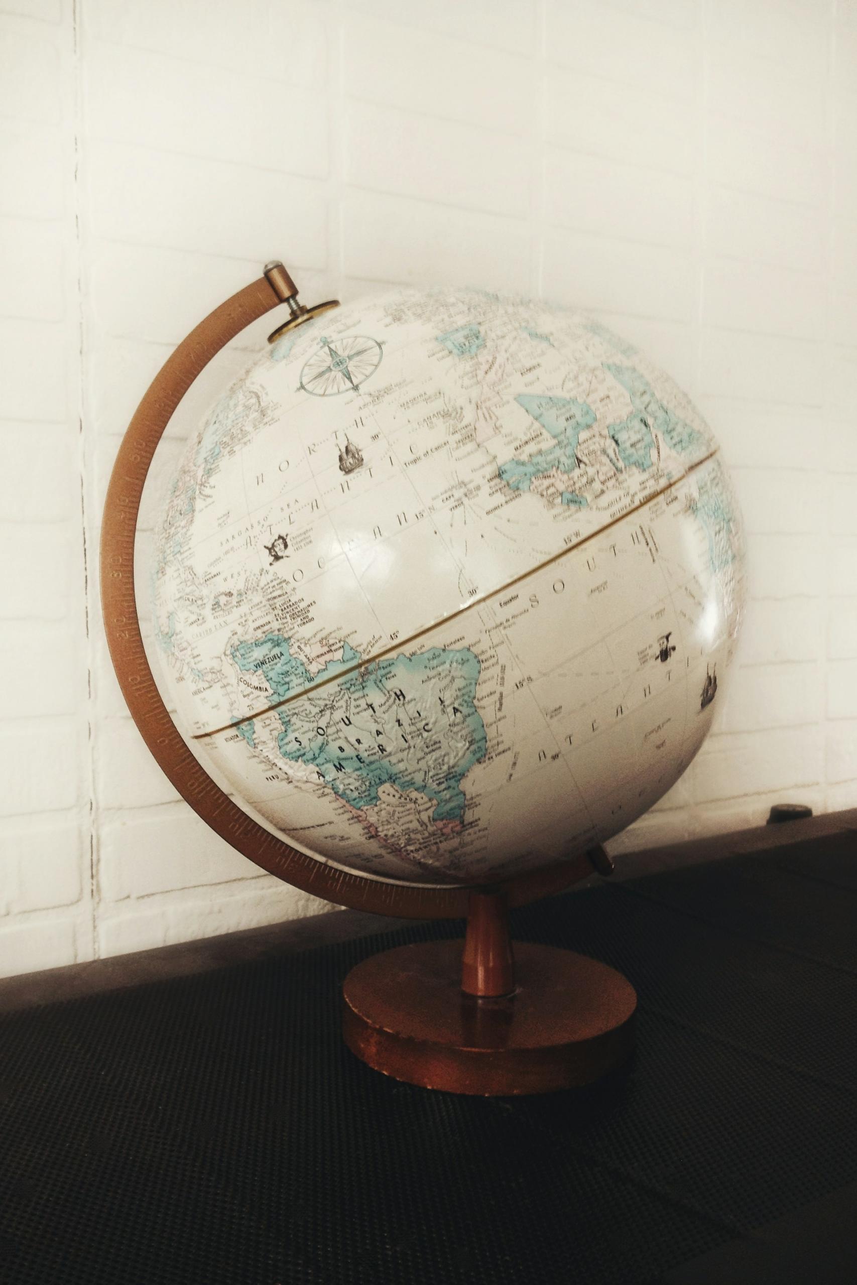 A globe on a wooden mount in front of a white brick wall.