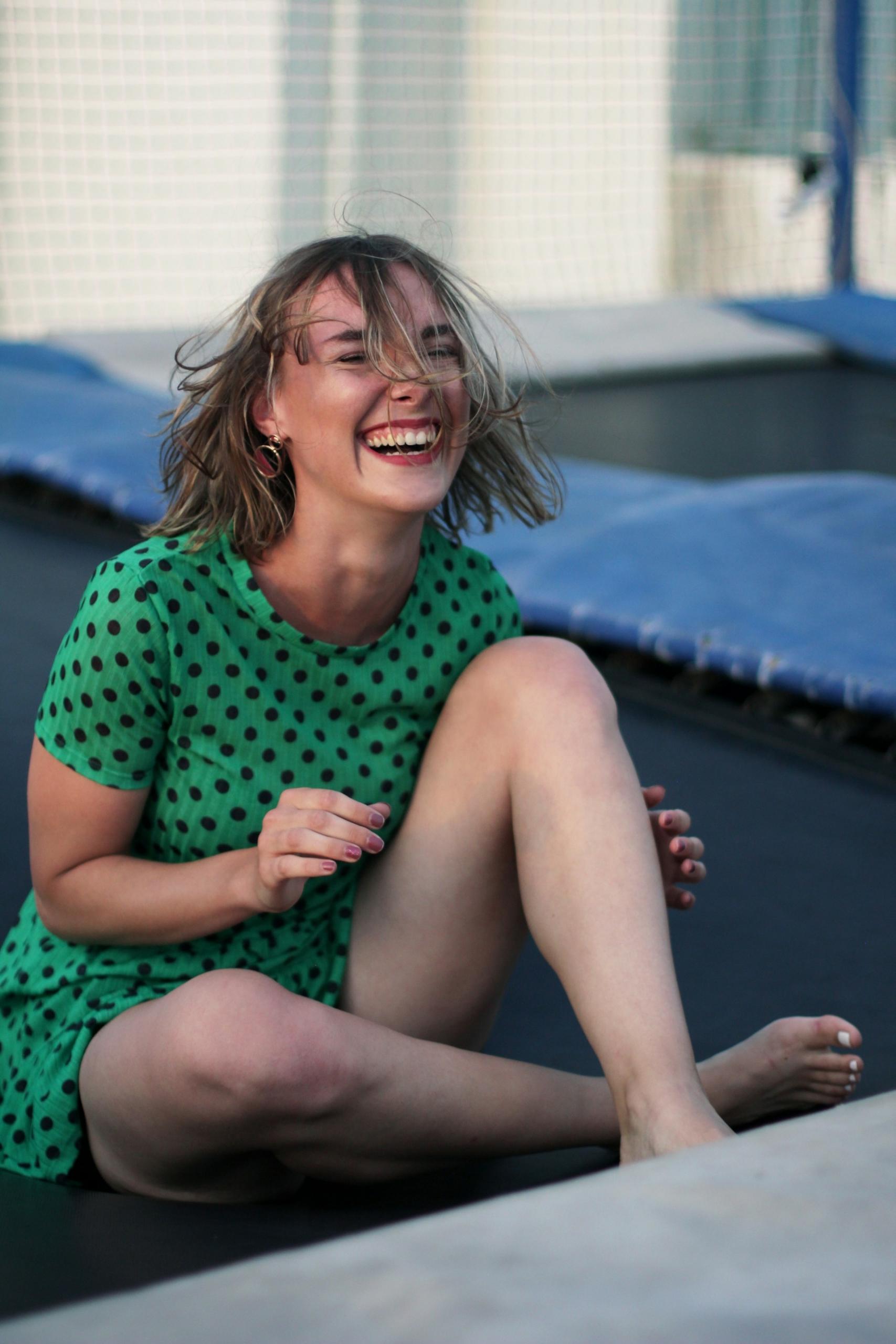A woman wearing green laughs while sitting on the floor.