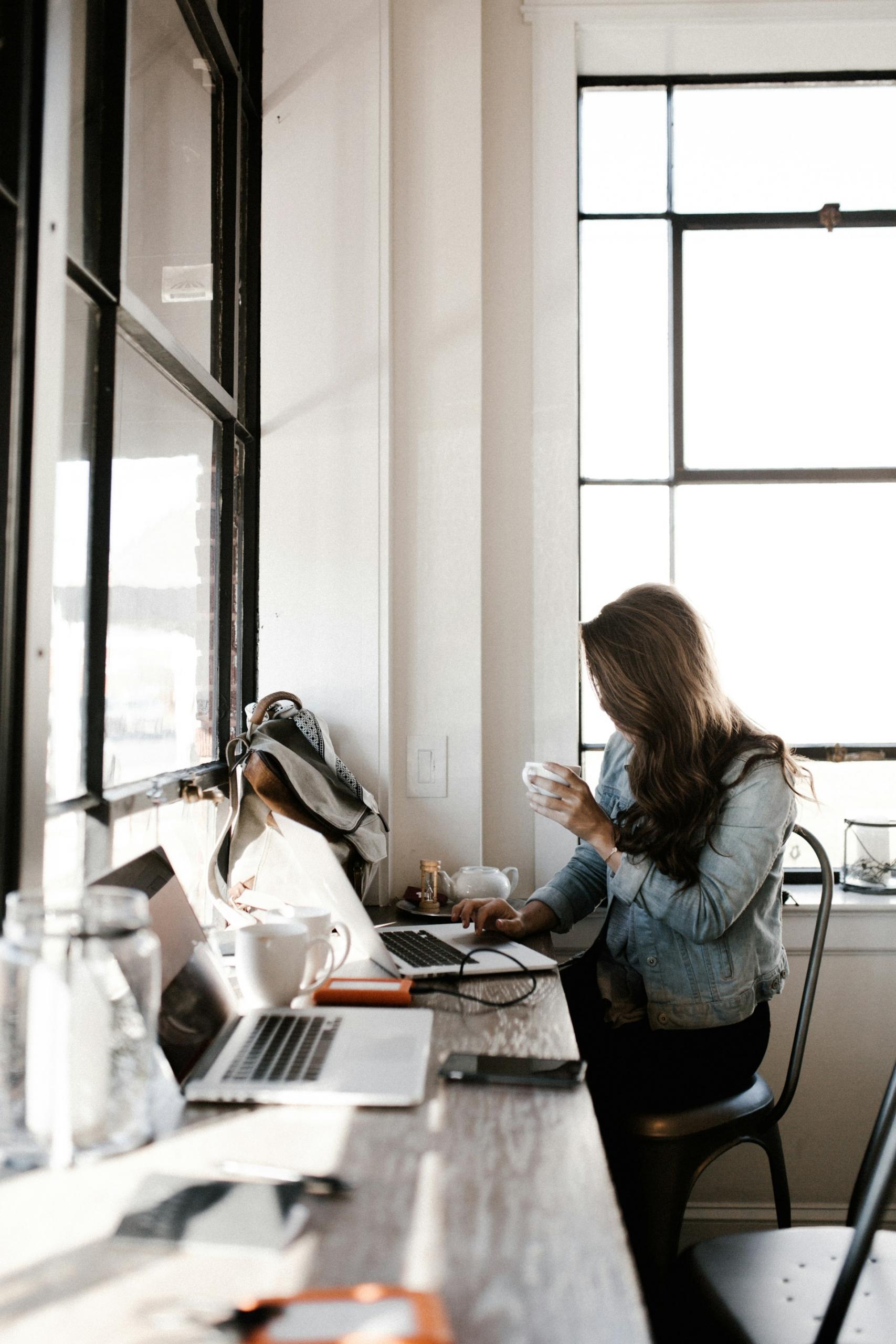 a woman sits at a table with her things in front of her and a cup in her hand.