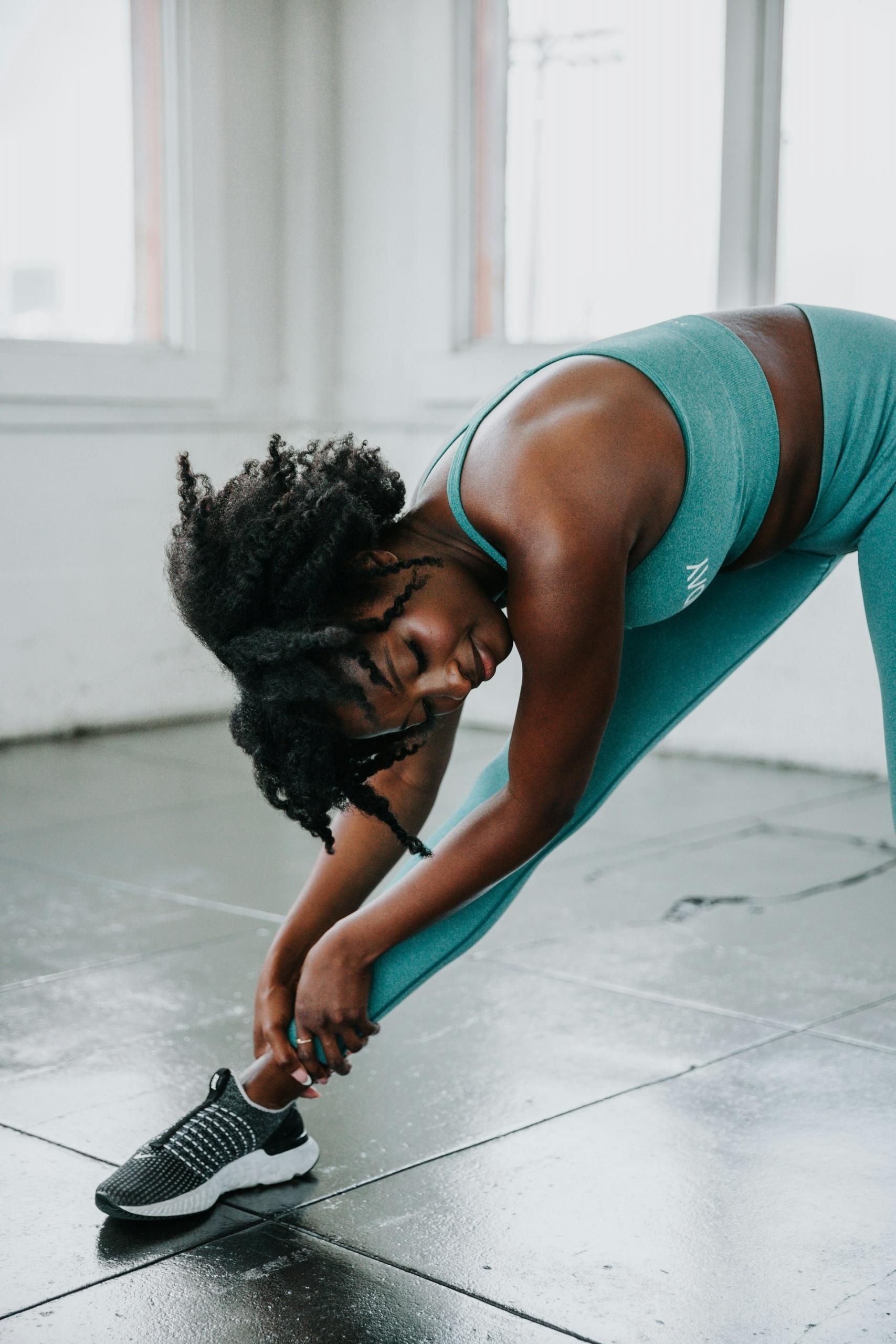 A woman wearing green workout gear stretches in a studio.