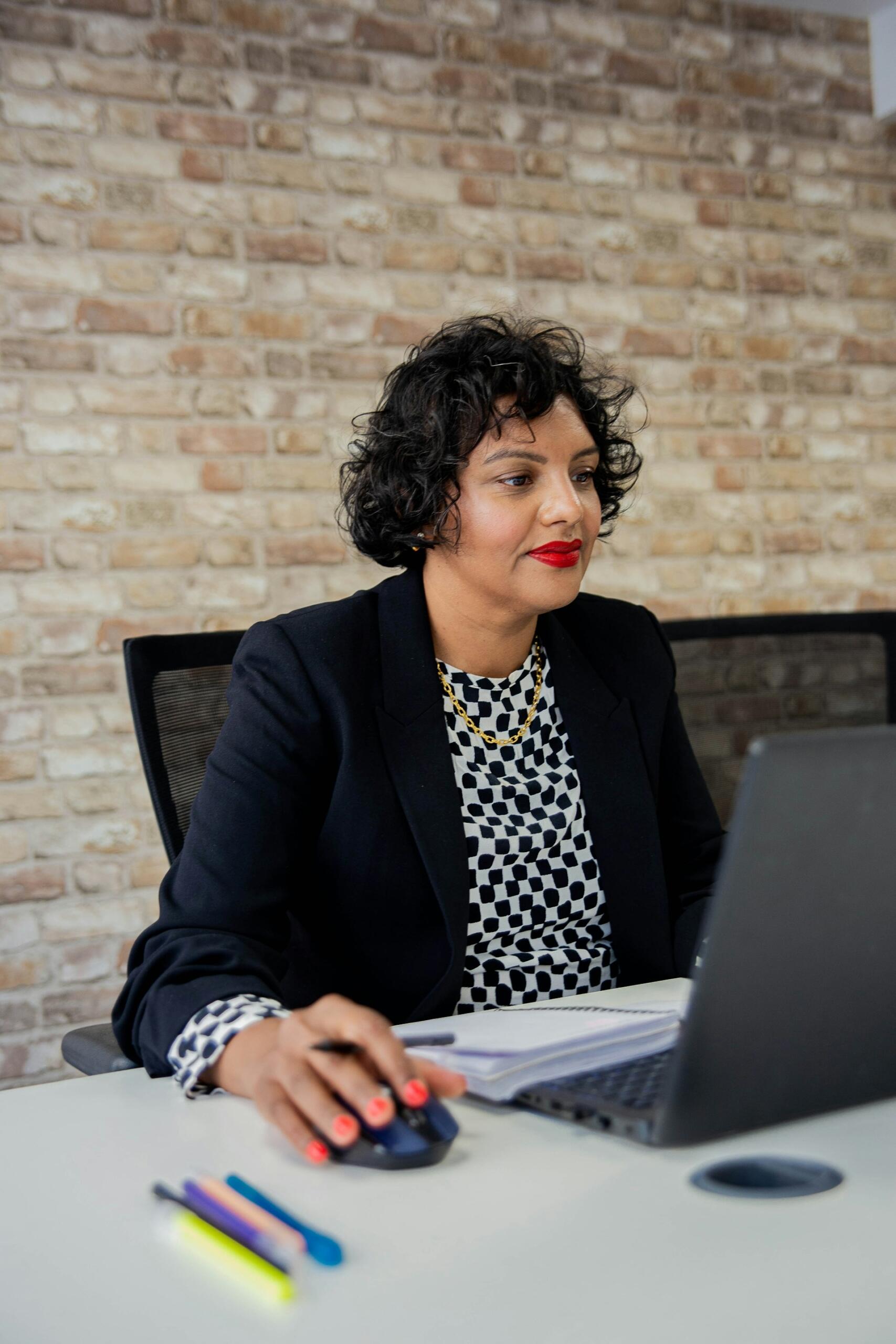 A woman wearing a blue jacket at a table in front of a computer.