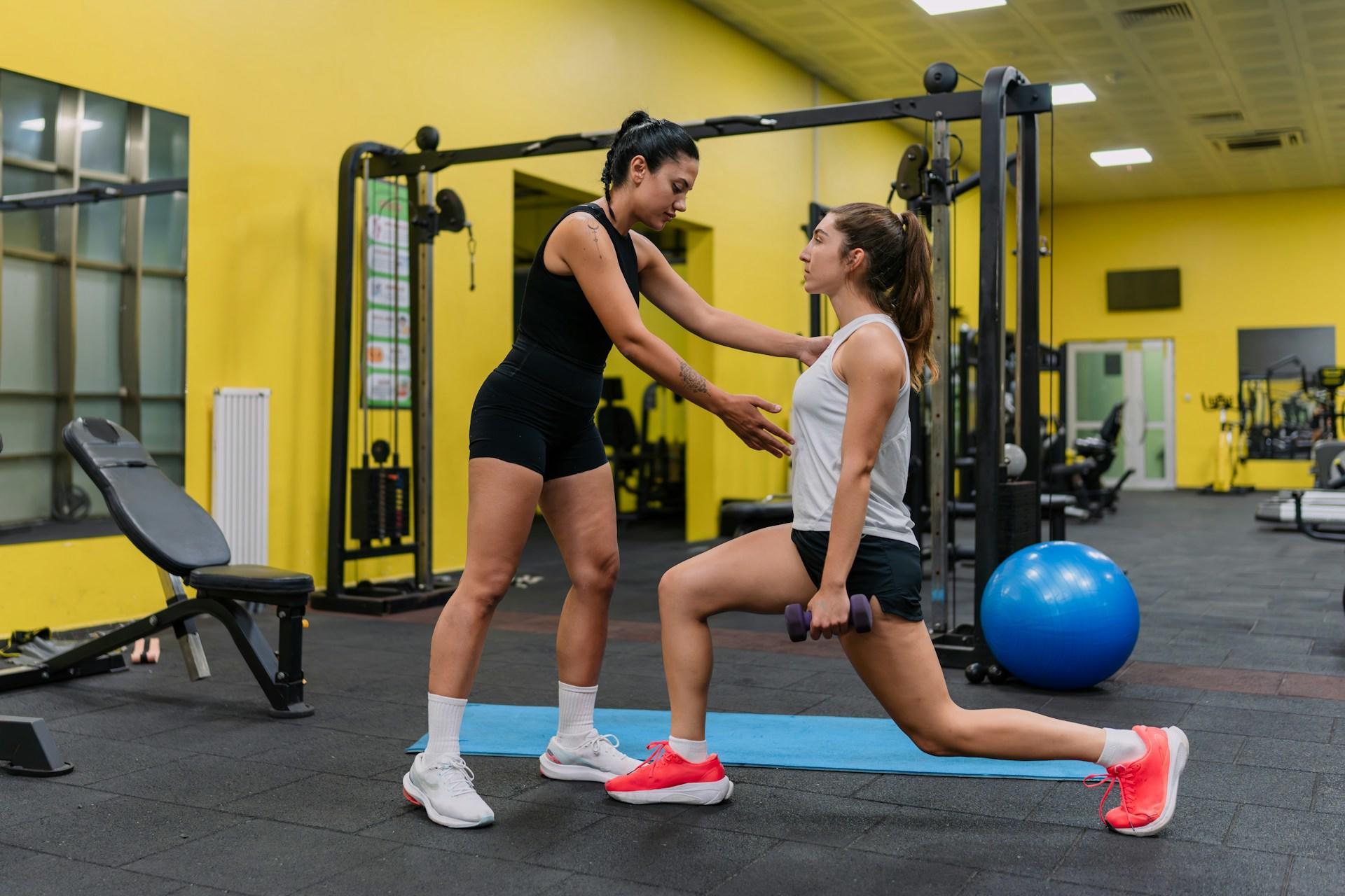 Two women in a gym, one showing the other how to work.