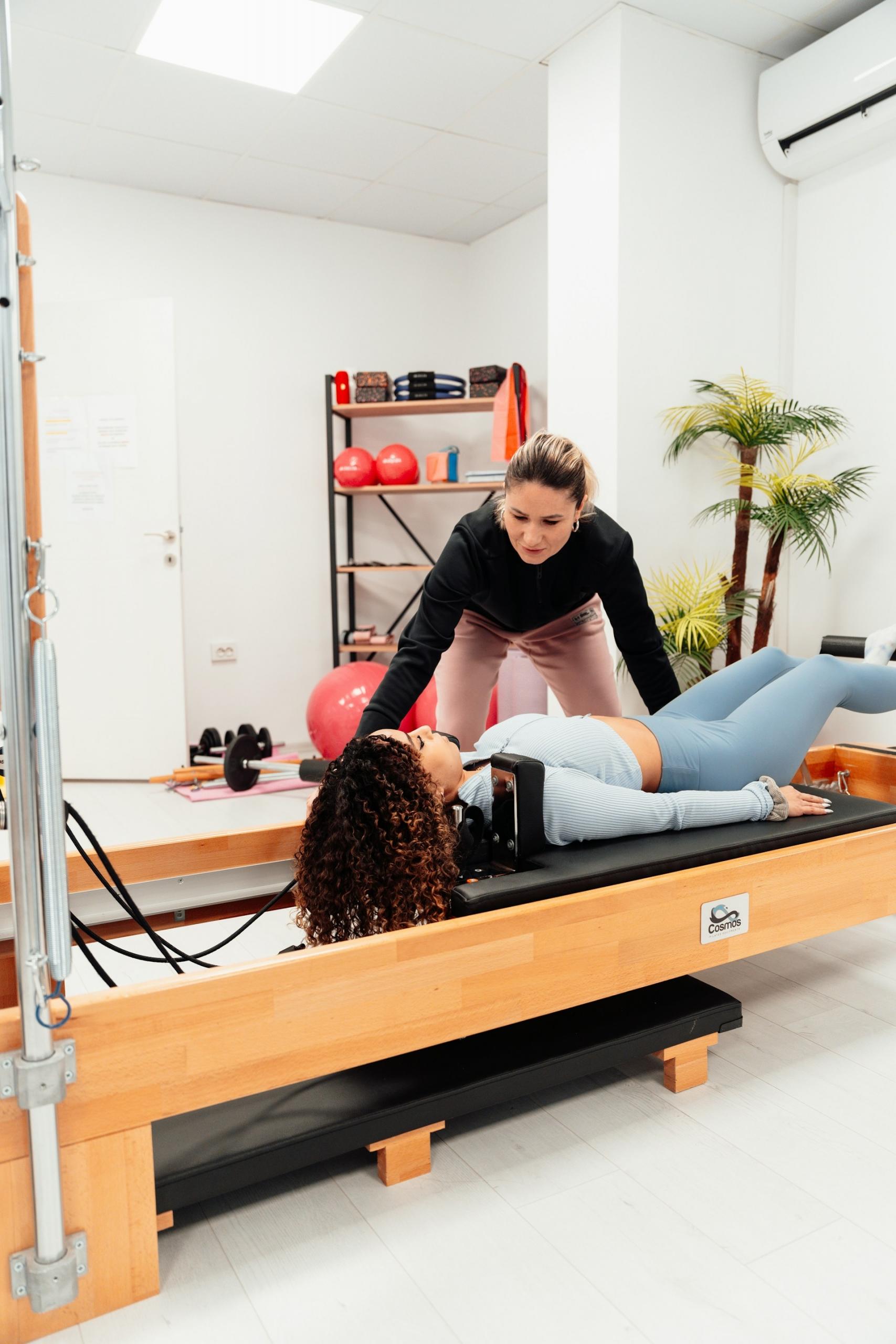 A woman on a Pilates table with a coach leaning over her.
