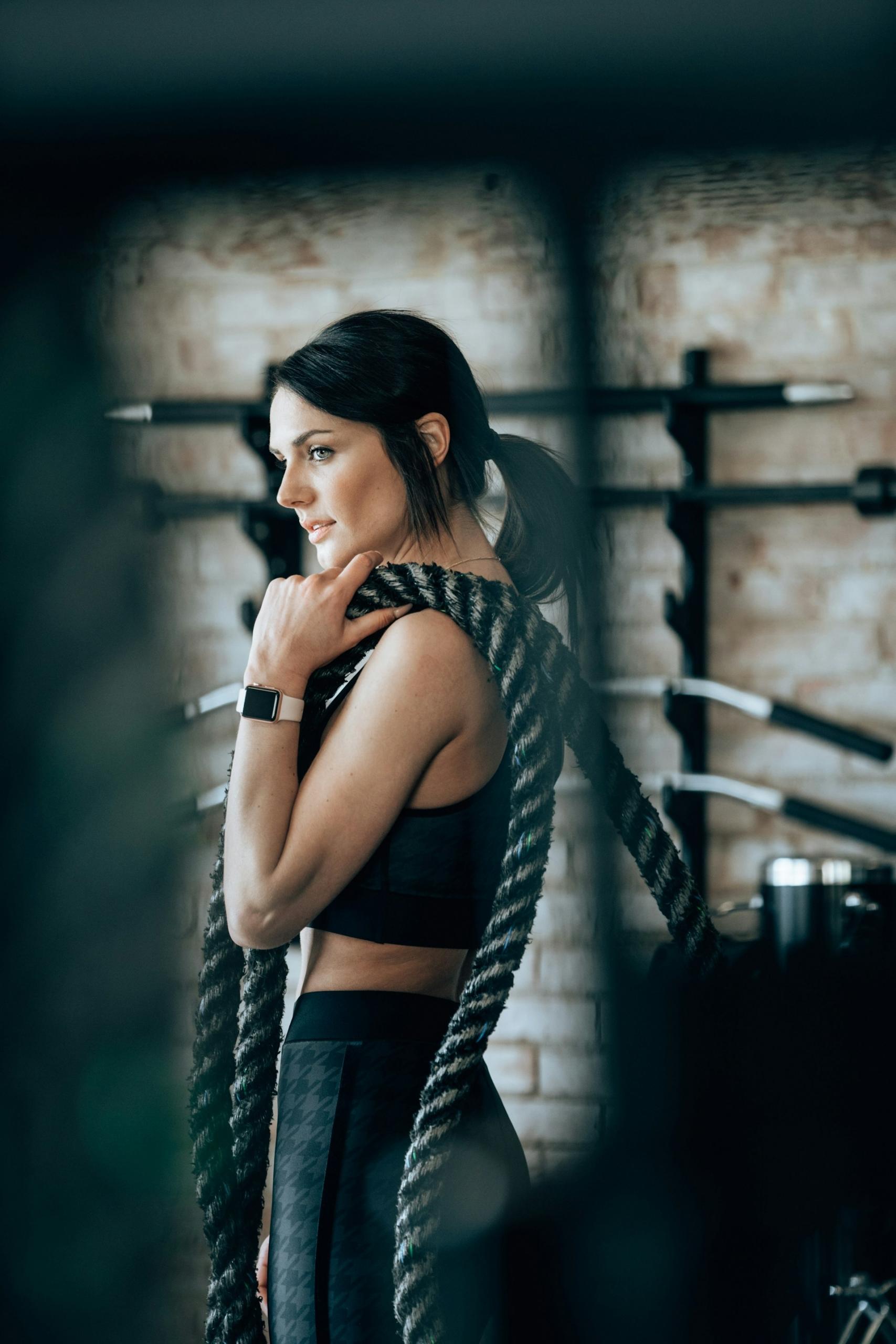 A woman in a gym with a heavy rope slung over her shoulder.