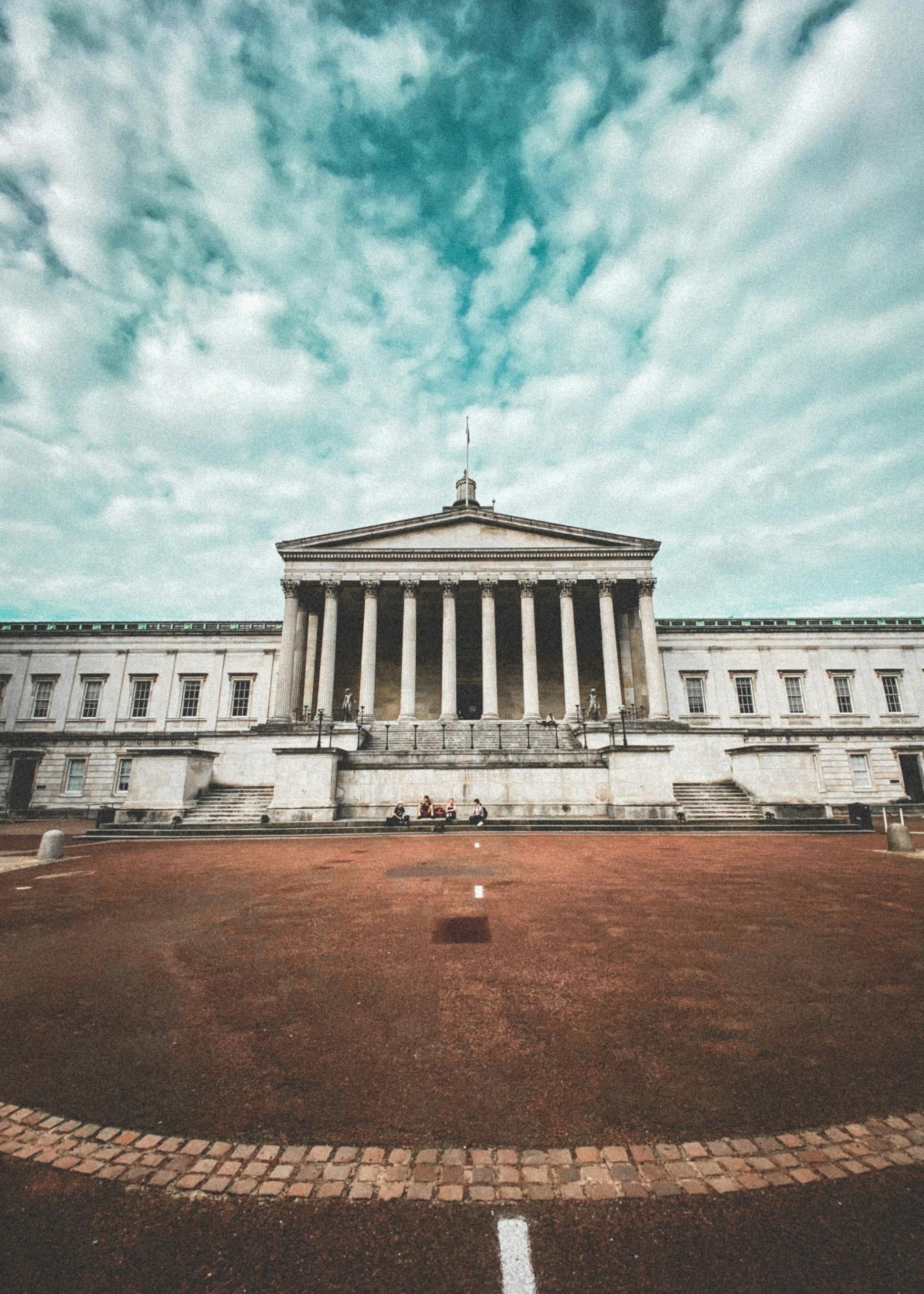 A stone building with columns across an open space on a cloudy day. 