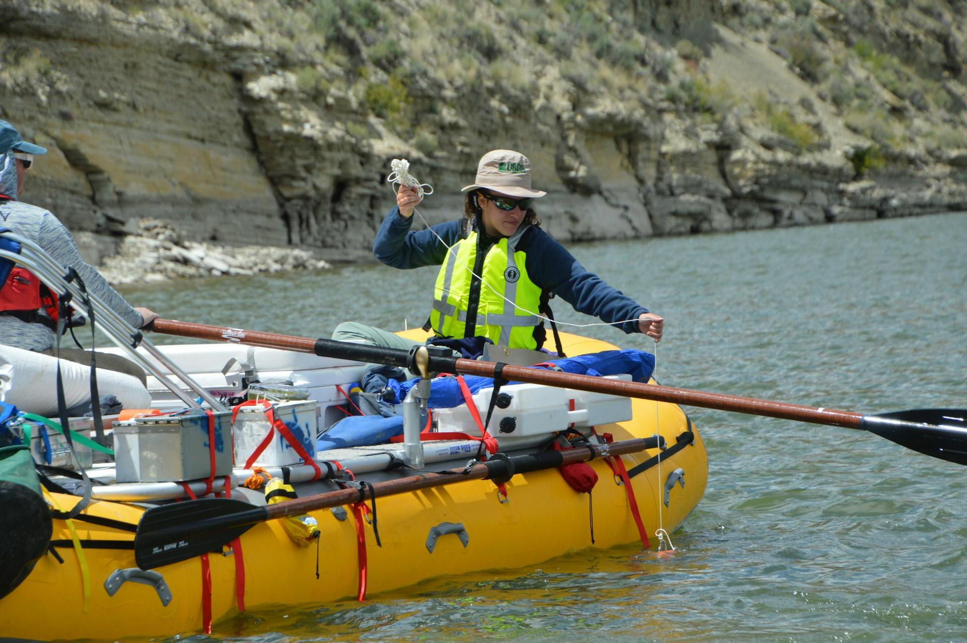 A person in a high-vis vest in a yellow inflatable boat on a river.