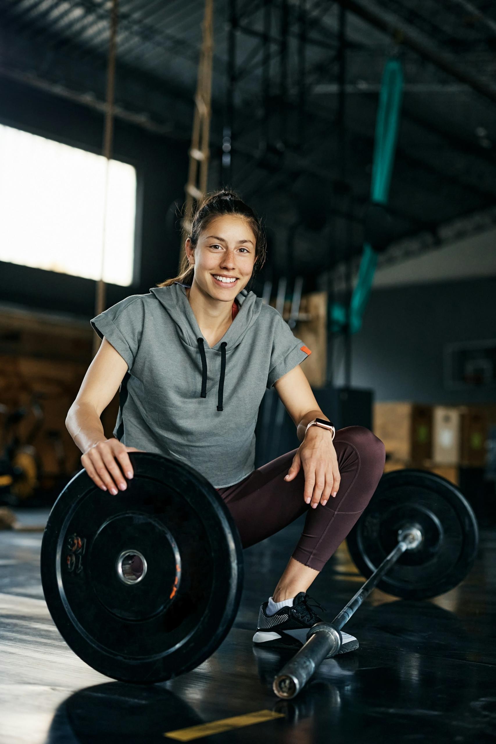 A woman kneels next to a barbell. 