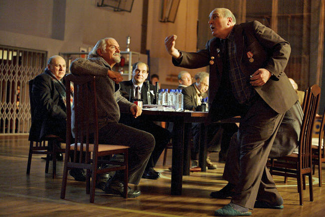 a group of man discussing something while sitting and another man standing up to explain something in excitement. 