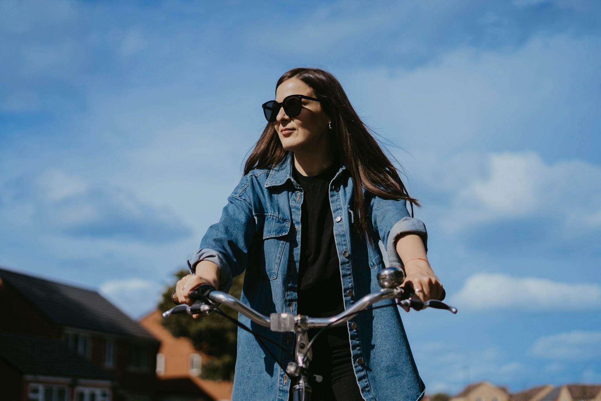 A woman with sunglasses on a bike on a sunny day. 